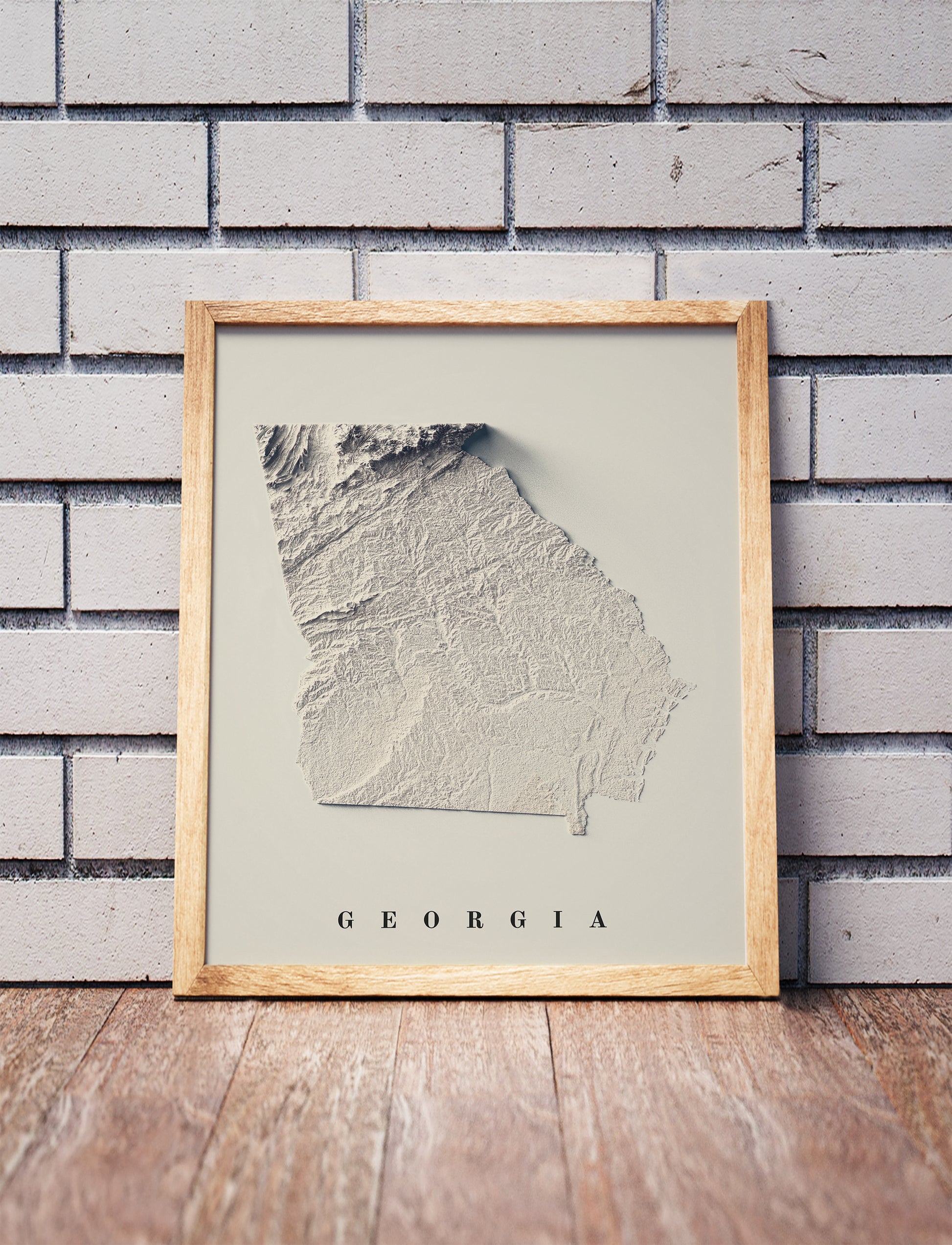 Georgia shaded relief map in a wooden frame. Realistic terrain art print for home decor, displayed against a brick wall