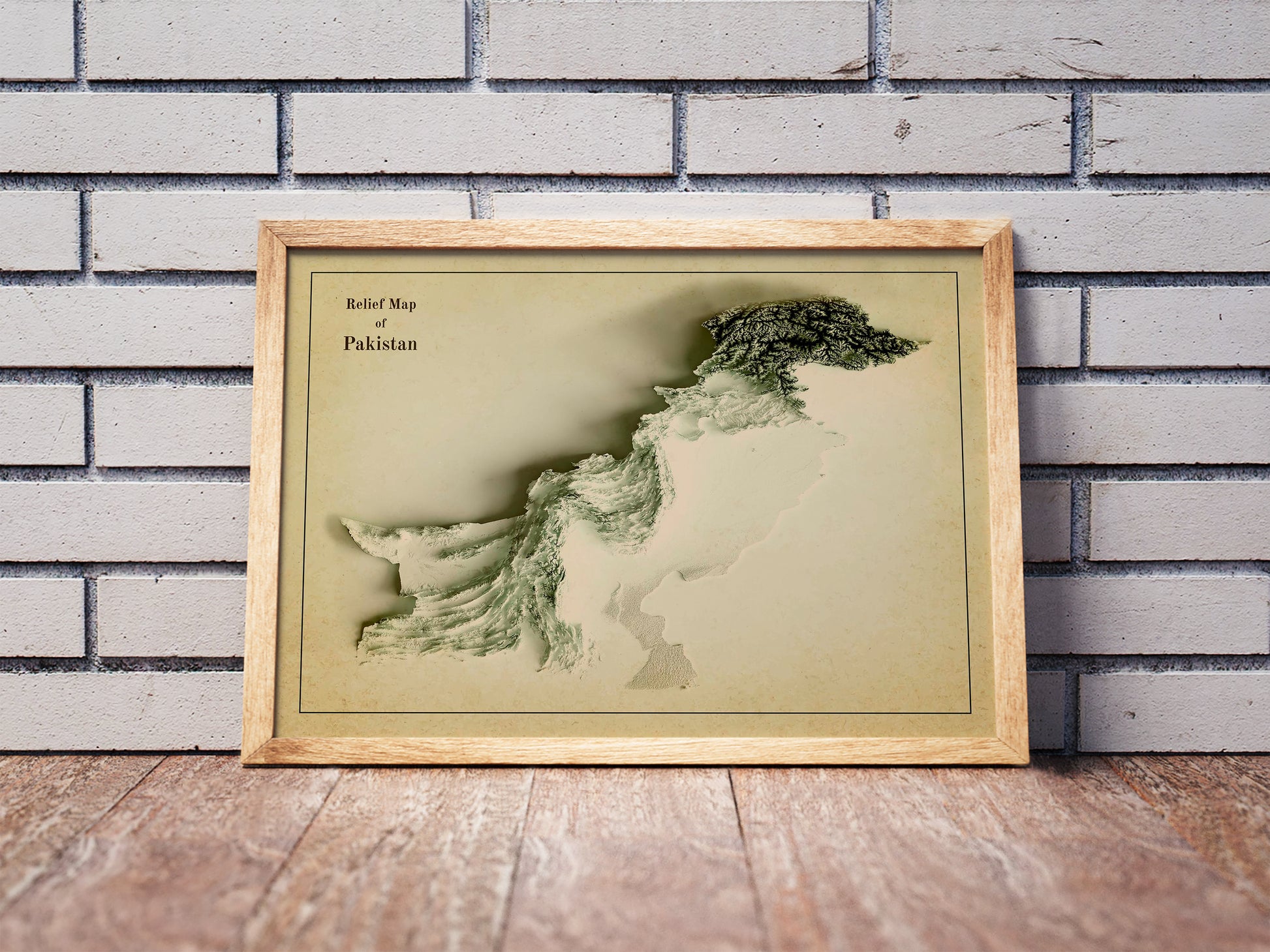 Vintage Pakistan shaded relief map in a wooden frame. Realistic terrain art print for home decor, displayed against a brick wall