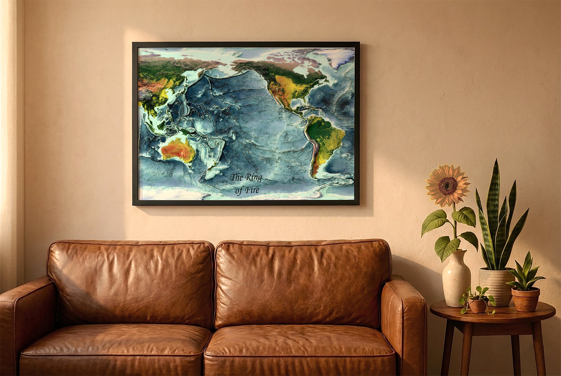 Ring of Fire relief map in a black frame above a brown leather sofa. Boho living room with warm sunlight, sunflower, and indoor plants on a wooden side table