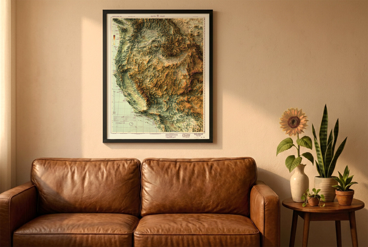 Western USA vintage relief map in a black frame above a brown leather sofa. Boho living room with warm sunlight, sunflower, and indoor plants on a wooden side table