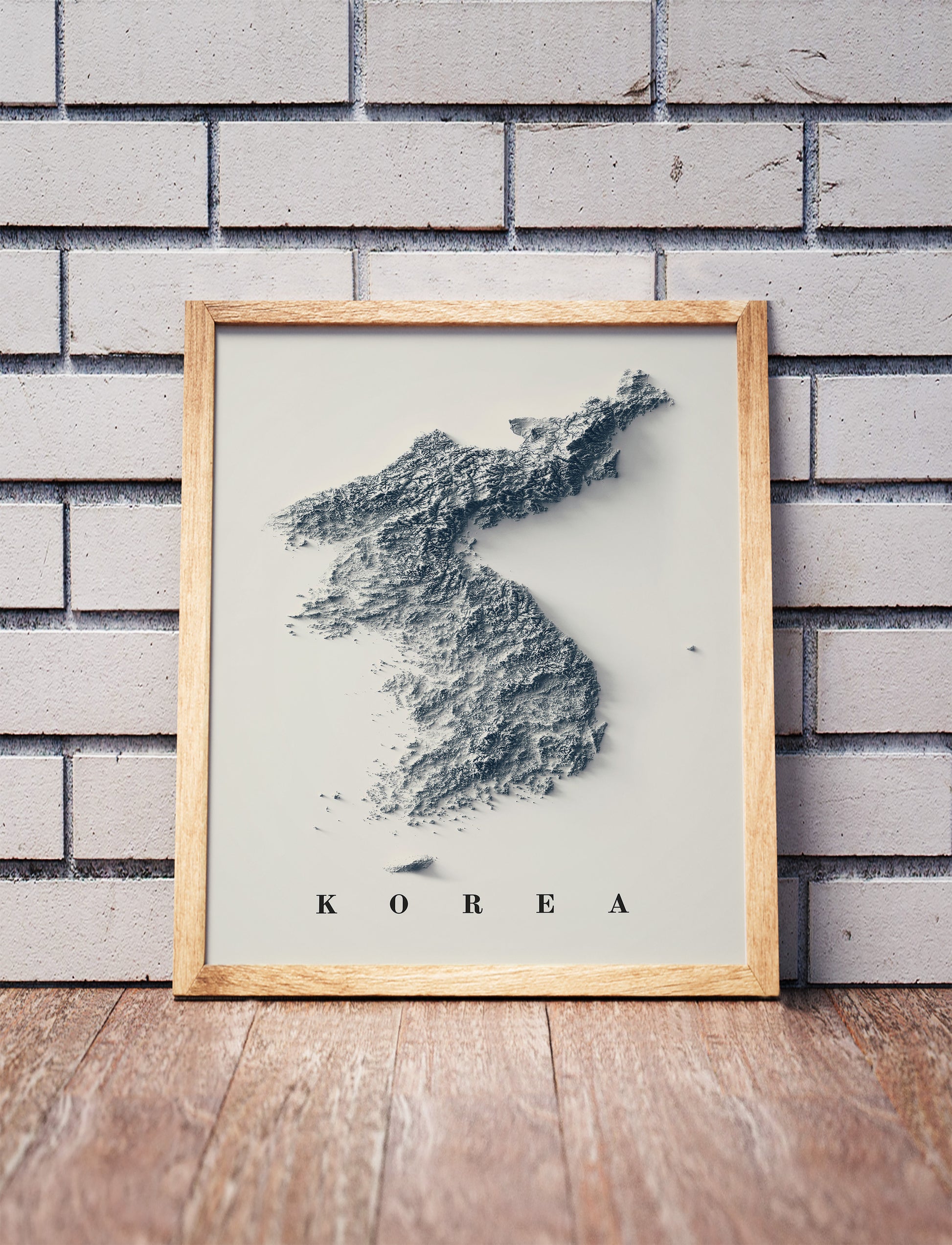 North and South Koreas shaded relief map in a wooden frame. Realistic terrain art print for home decor, displayed against a brick wall