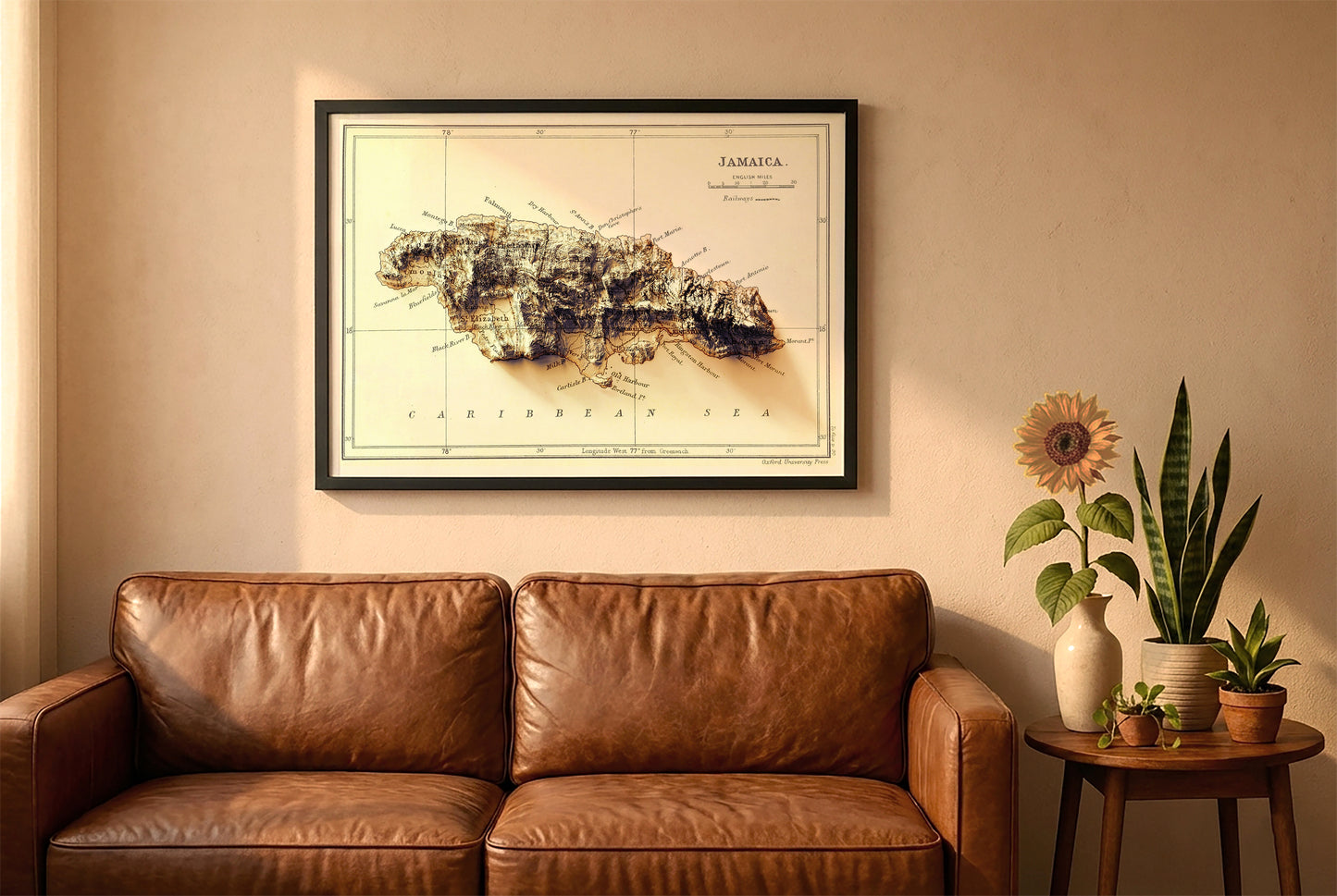 Jamaica vintage relief map in a black frame above a brown leather sofa. Boho living room with warm sunlight, sunflower, and indoor plants on a wooden side table