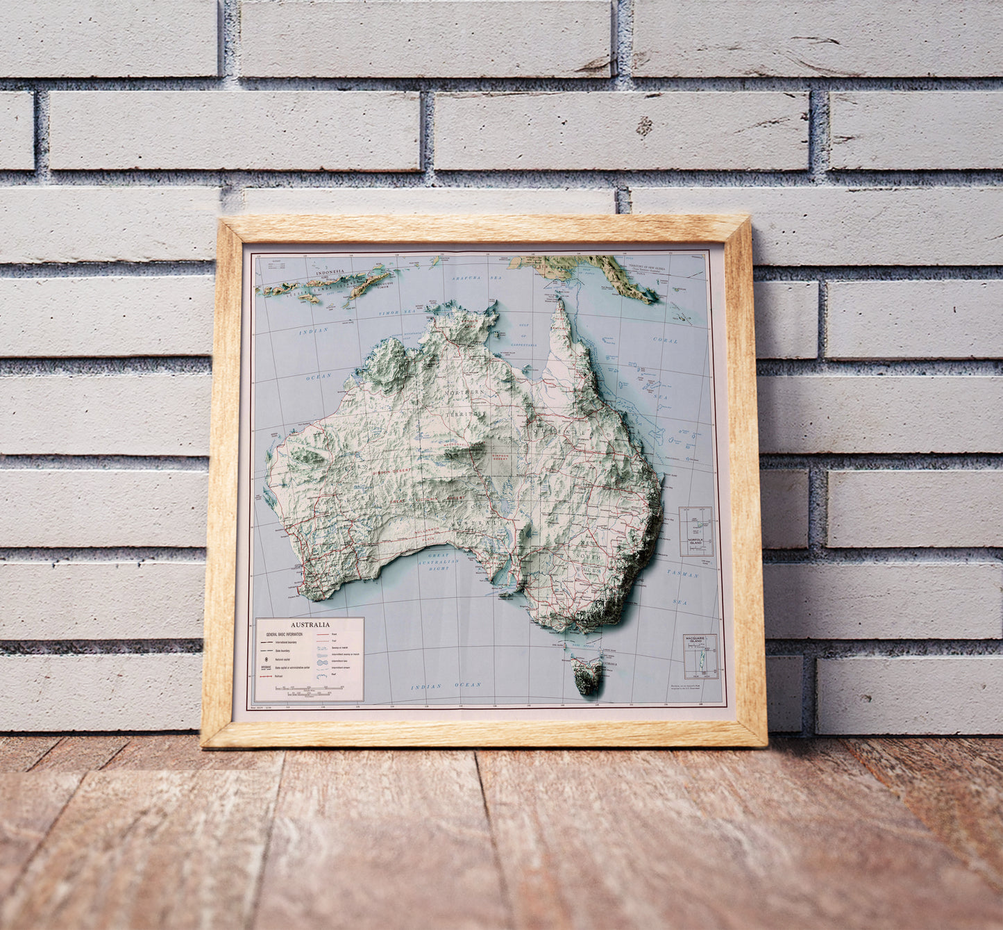 Vintage Australia shaded relief map in a wooden frame. Realistic terrain art print for home decor, displayed against a brick wall