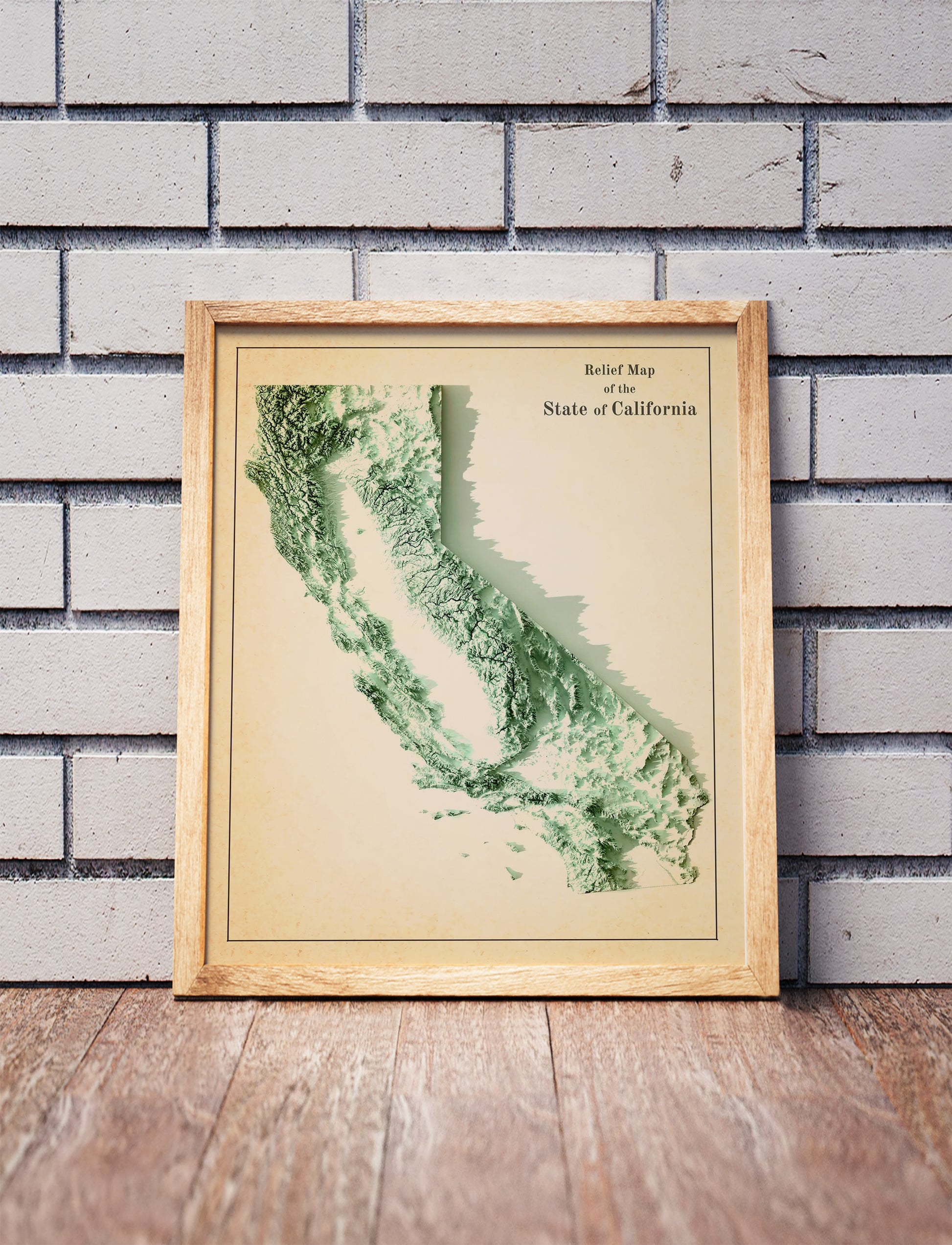 Vintage California shaded relief map in a wooden frame. Realistic terrain art print for home decor, displayed against a brick wall