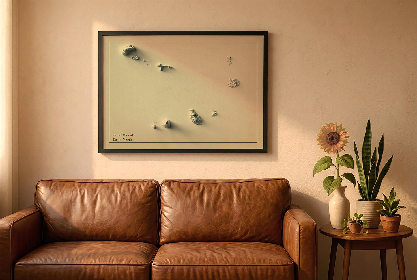 Cape Verde vintage relief map in a black frame above a brown leather sofa. Boho living room with warm sunlight, sunflower, and indoor plants on a wooden side table
