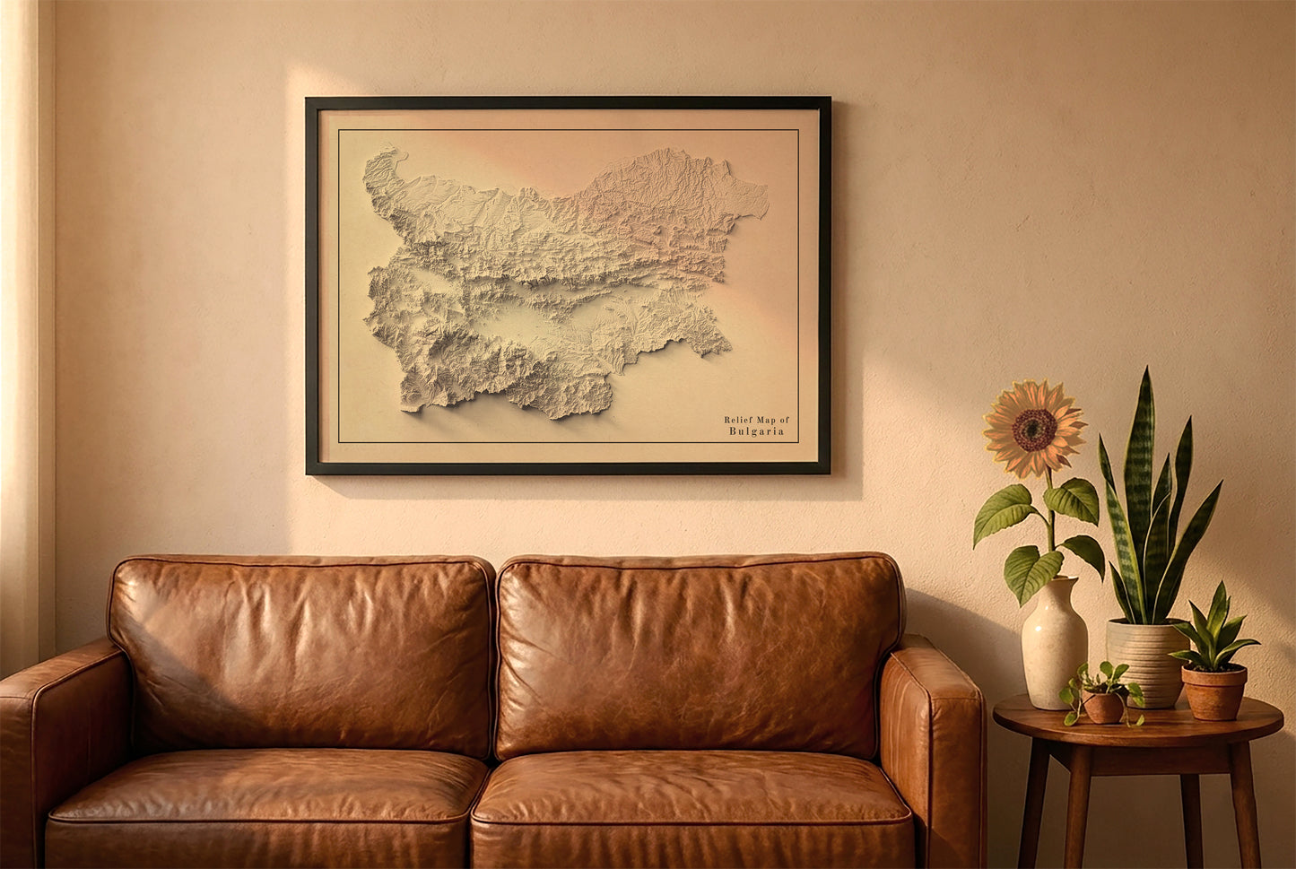 Bulgaria vintage relief map in a black frame above a brown leather sofa. Boho living room with warm sunlight, sunflower, and indoor plants on a wooden side table