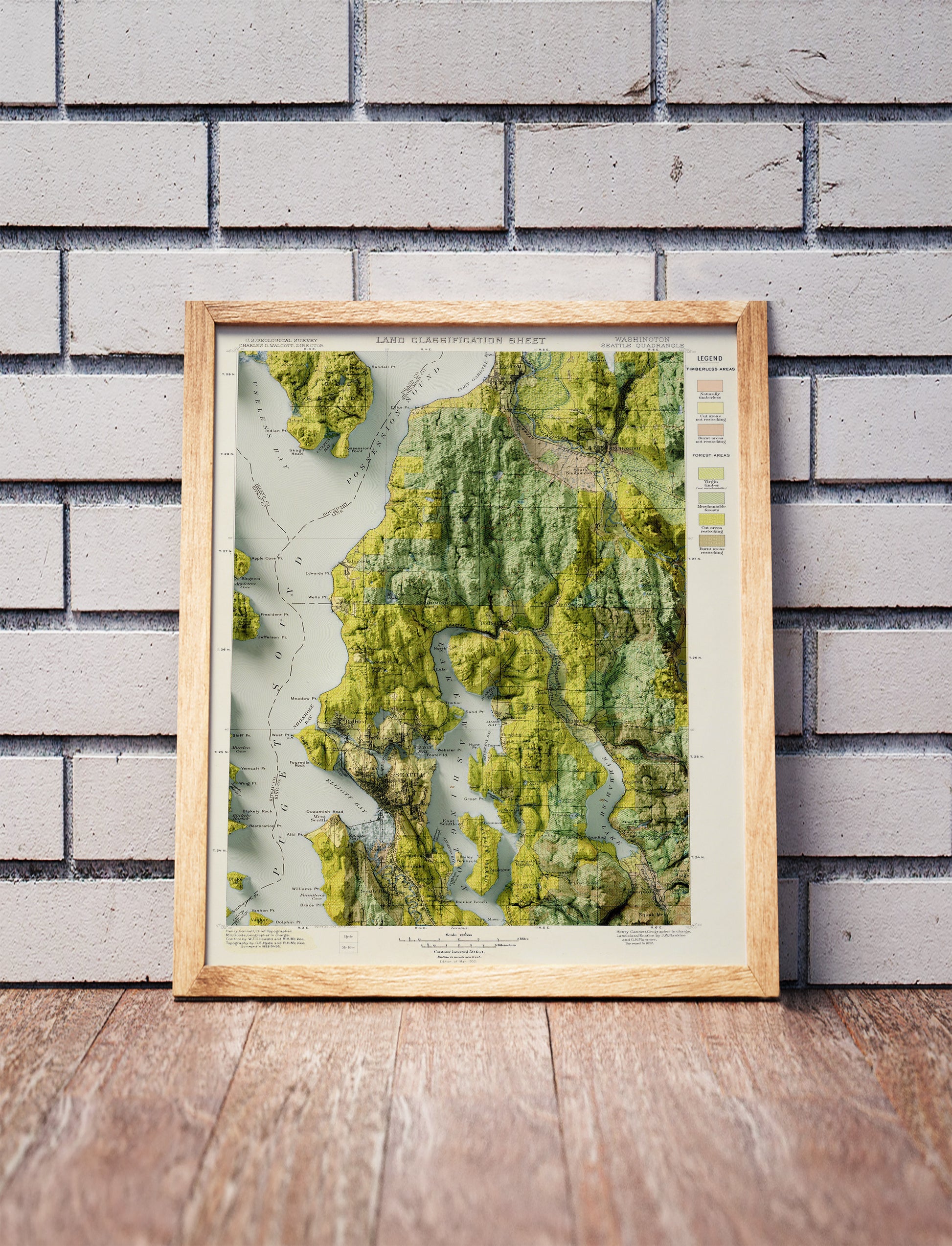 Vintage Seattle shaded relief map in a wooden frame. Realistic terrain art print for home decor, displayed against a brick wall