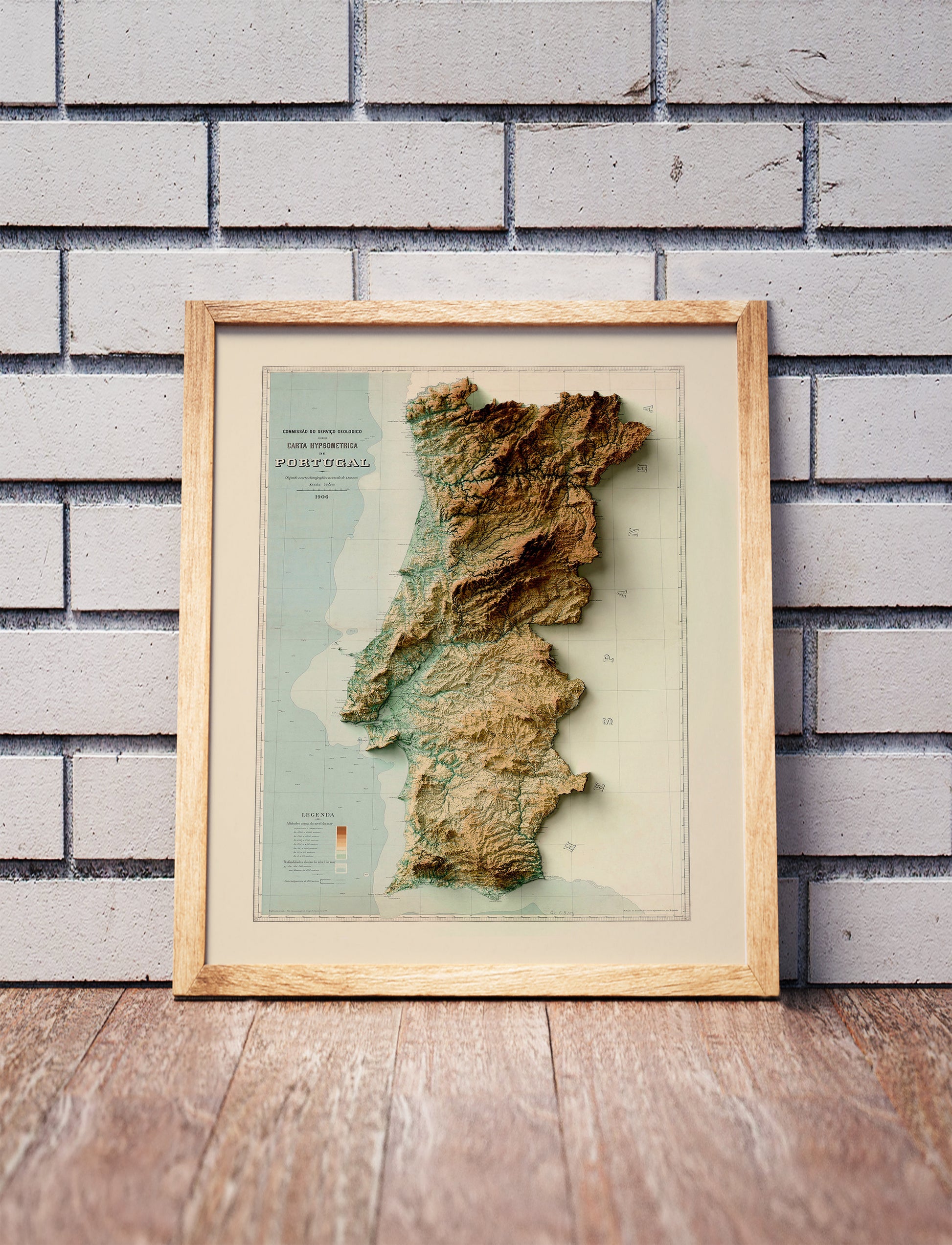 Vintage Portugal shaded relief map in a wooden frame. Realistic terrain art print for home decor, displayed against a brick wall