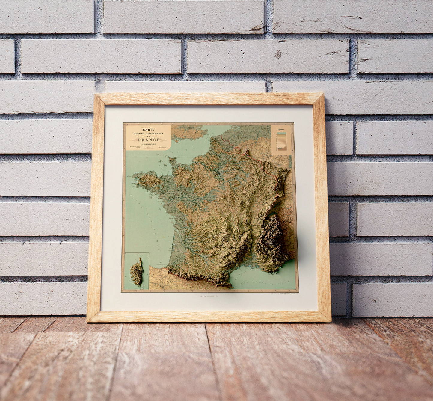 Vintage France shaded relief map in a wooden frame. Realistic terrain art print for home decor, displayed against a brick wall