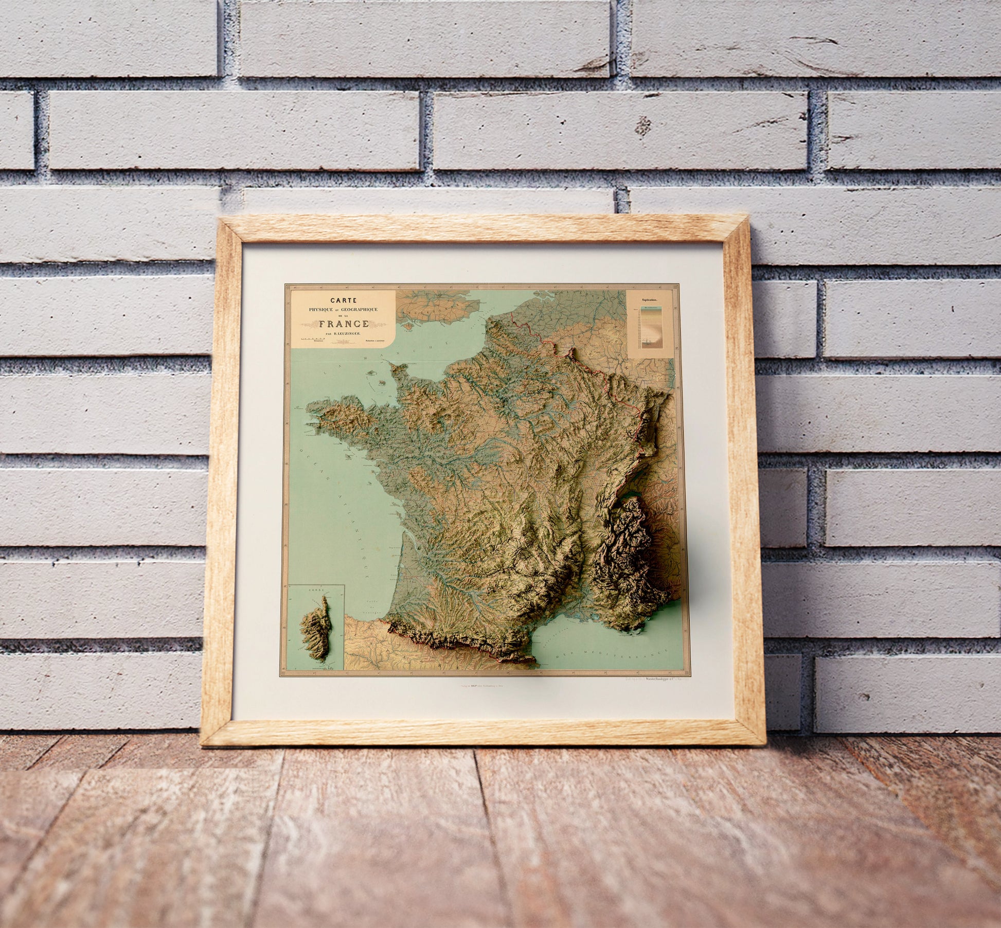 Vintage France shaded relief map in a wooden frame. Realistic terrain art print for home decor, displayed against a brick wall