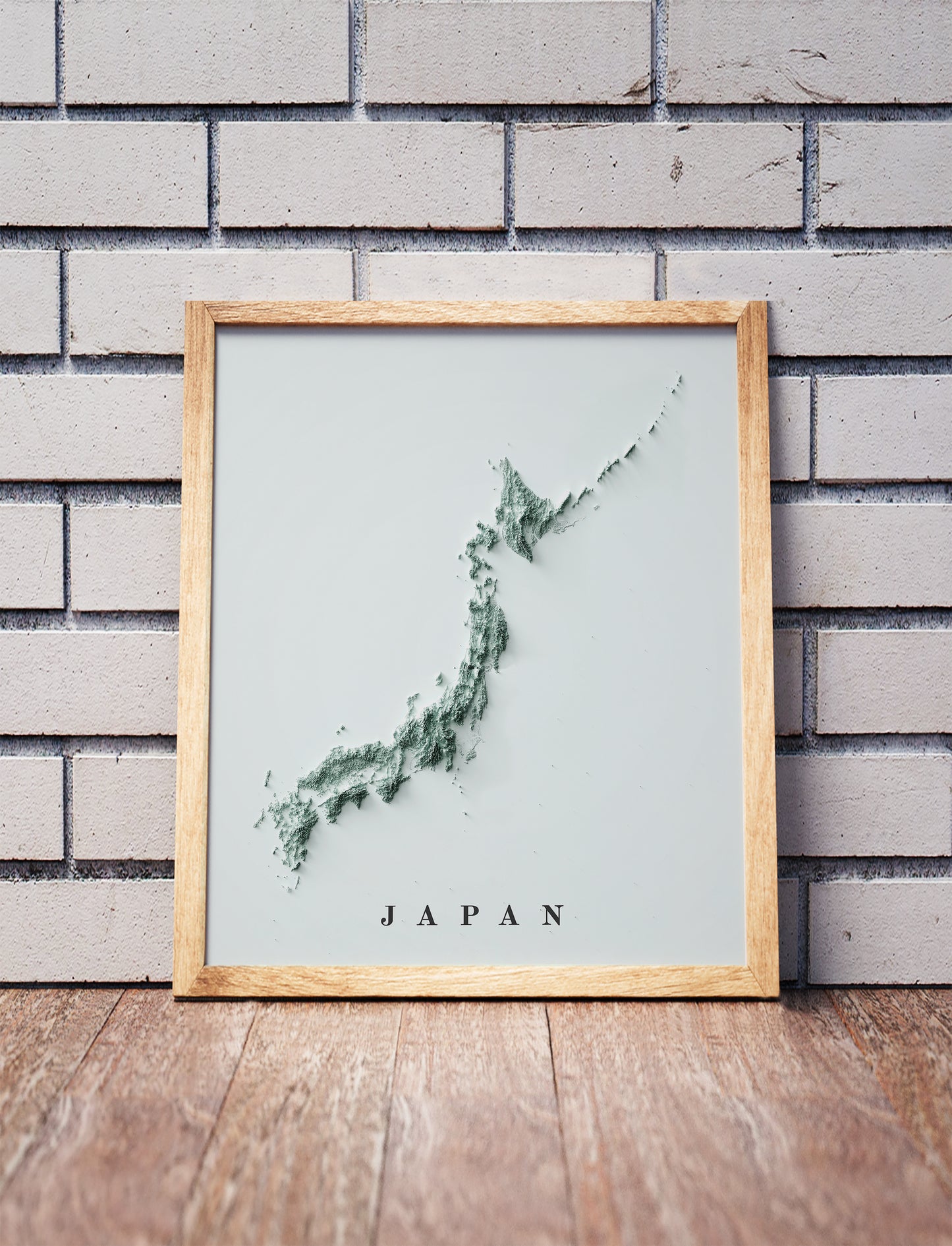 Japan shaded relief map in a wooden frame. Realistic terrain art print for home decor, displayed against a brick wall
