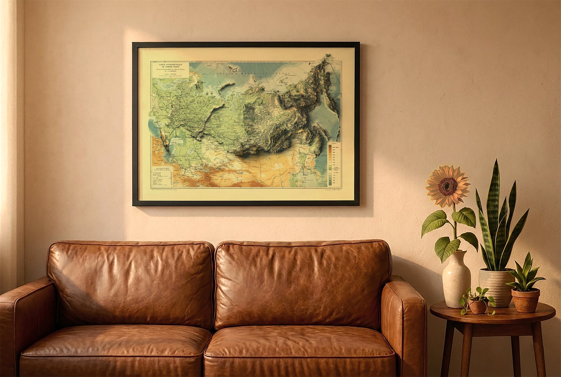 Russia vintage relief map in a black frame above a brown leather sofa. Boho living room with warm sunlight, sunflower, and indoor plants on a wooden side table