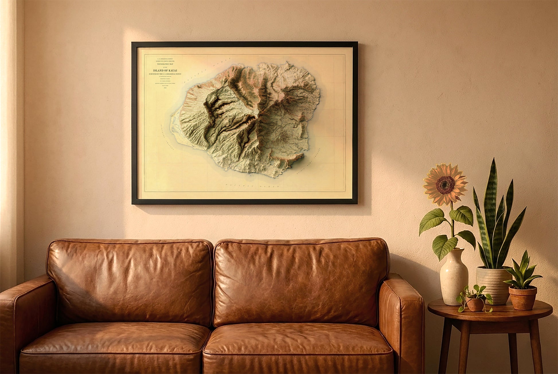 Kauai, Hawaii, vintage relief map in a black frame above a brown leather sofa. Boho living room with warm sunlight, sunflower, and indoor plants on a wooden side table