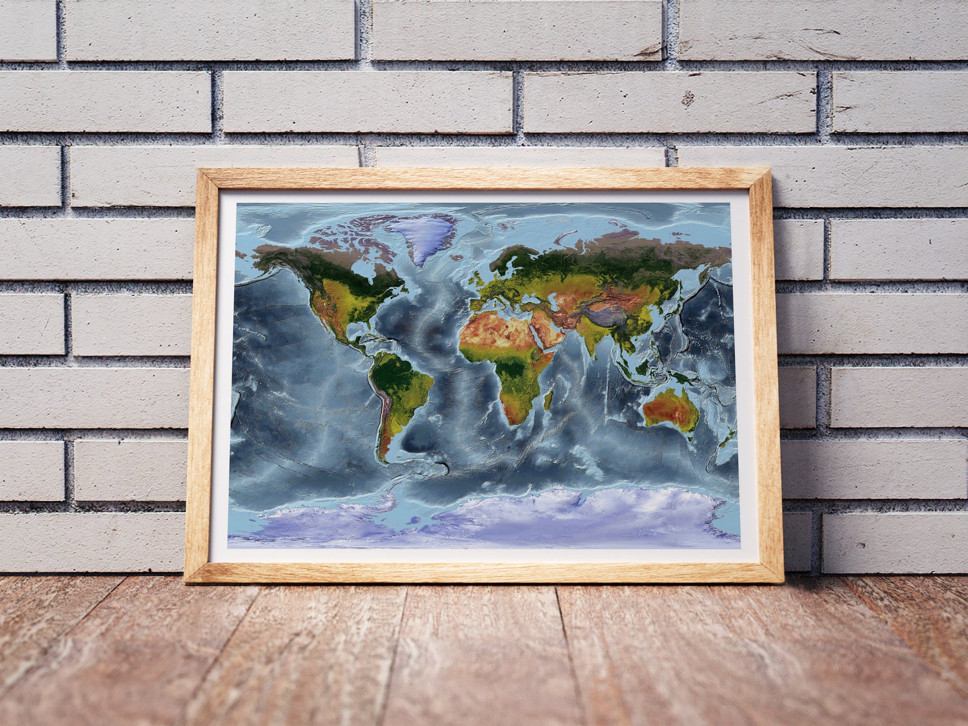 Gall Stereographic projection shaded relief world map in a wooden frame. Realistic terrain art print for home decor, displayed against a brick wall