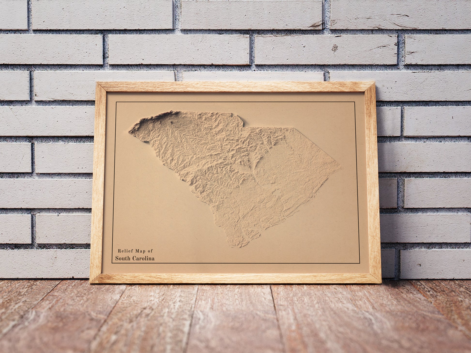 Vintage South Carolina shaded relief map in a wooden frame. Realistic terrain art print for home decor, displayed against a brick wall