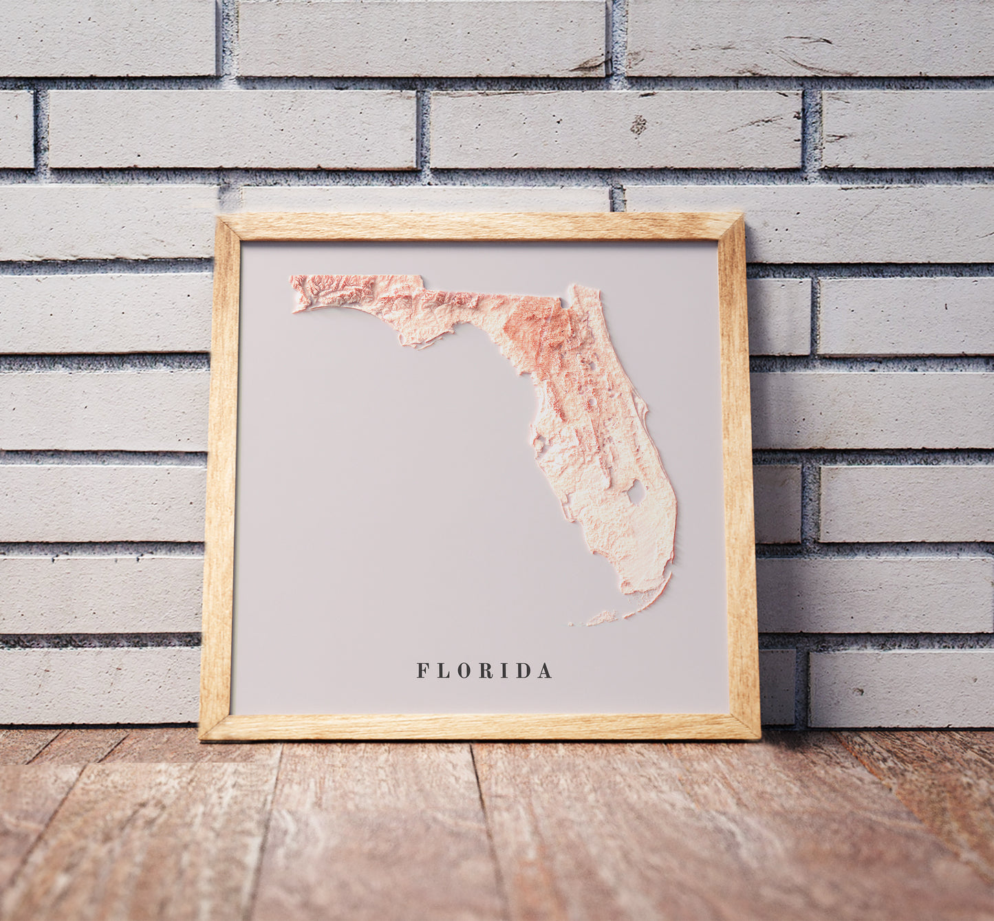 Florida shaded relief map in a wooden frame. Realistic terrain art print for home decor, displayed against a brick wall