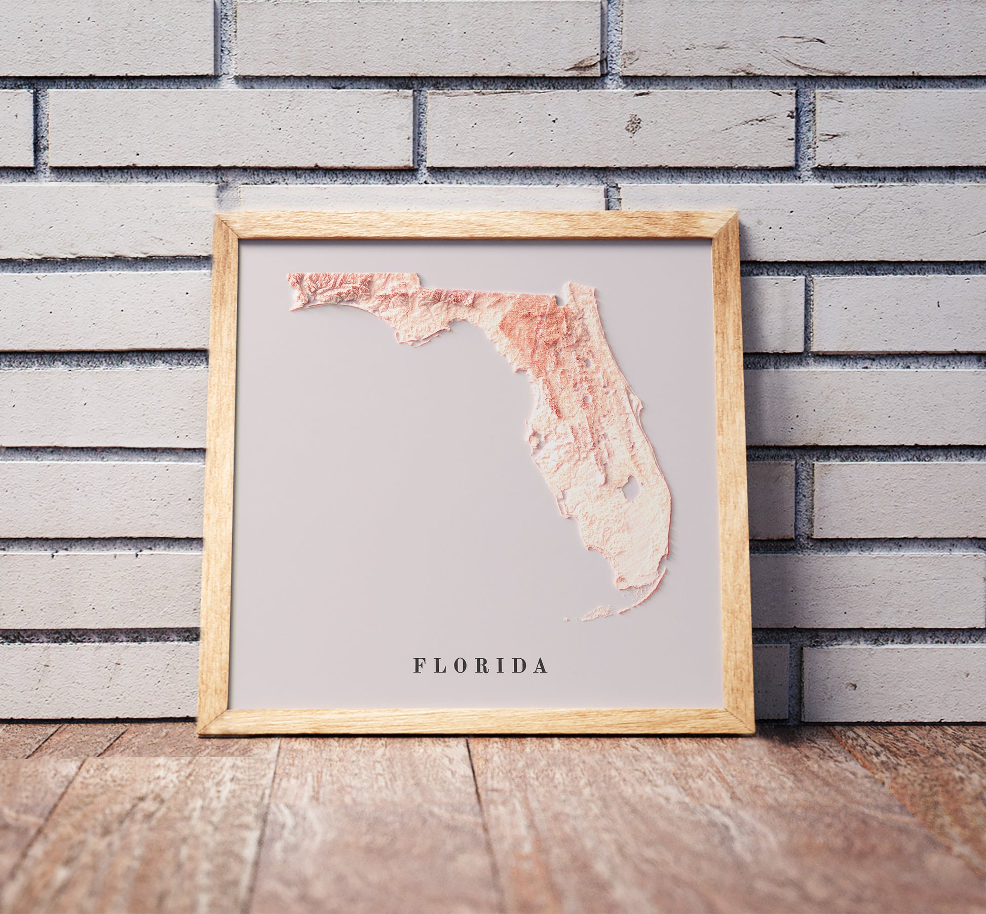 Florida shaded relief map in a wooden frame. Realistic terrain art print for home decor, displayed against a brick wall