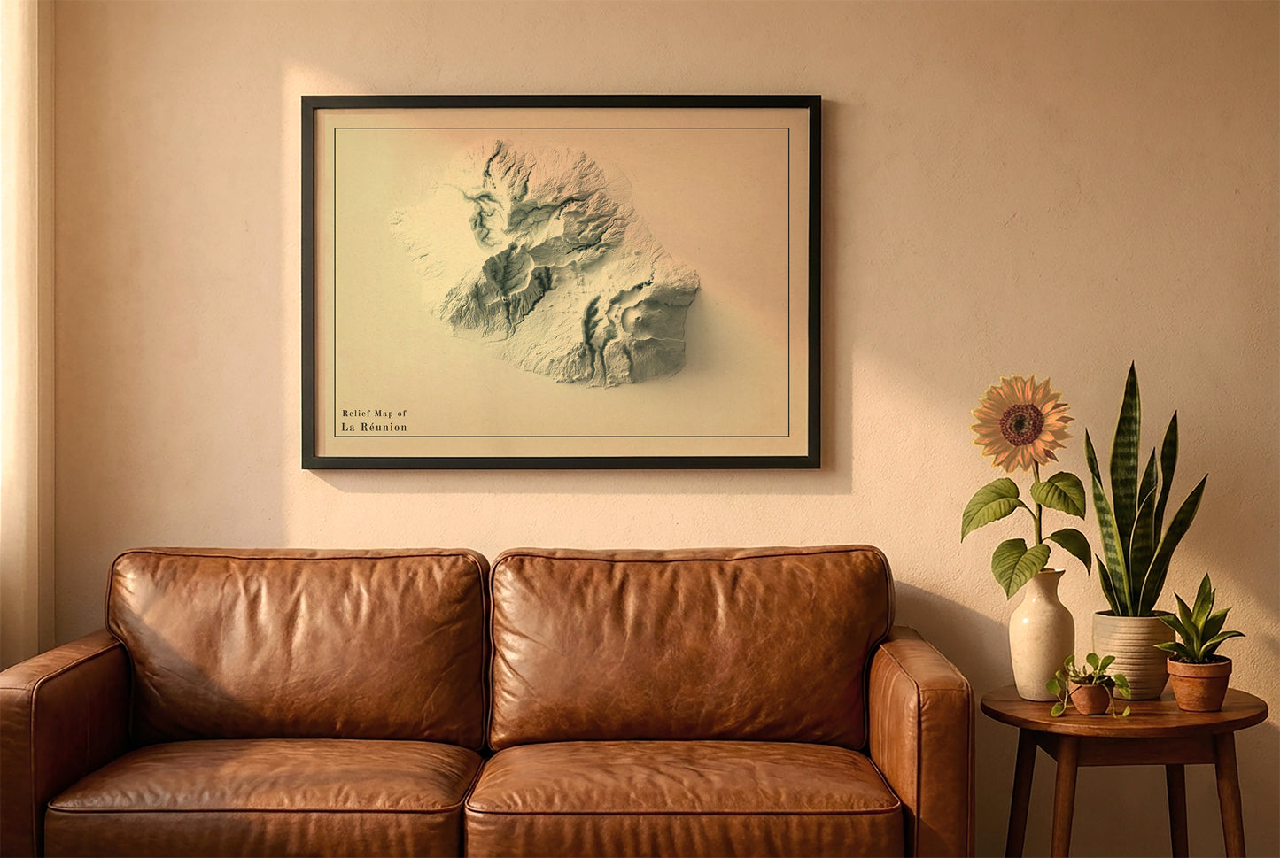 Reunion, France, vintage relief map in a black frame above a brown leather sofa. Boho living room with warm sunlight, sunflower, and indoor plants on a wooden side table