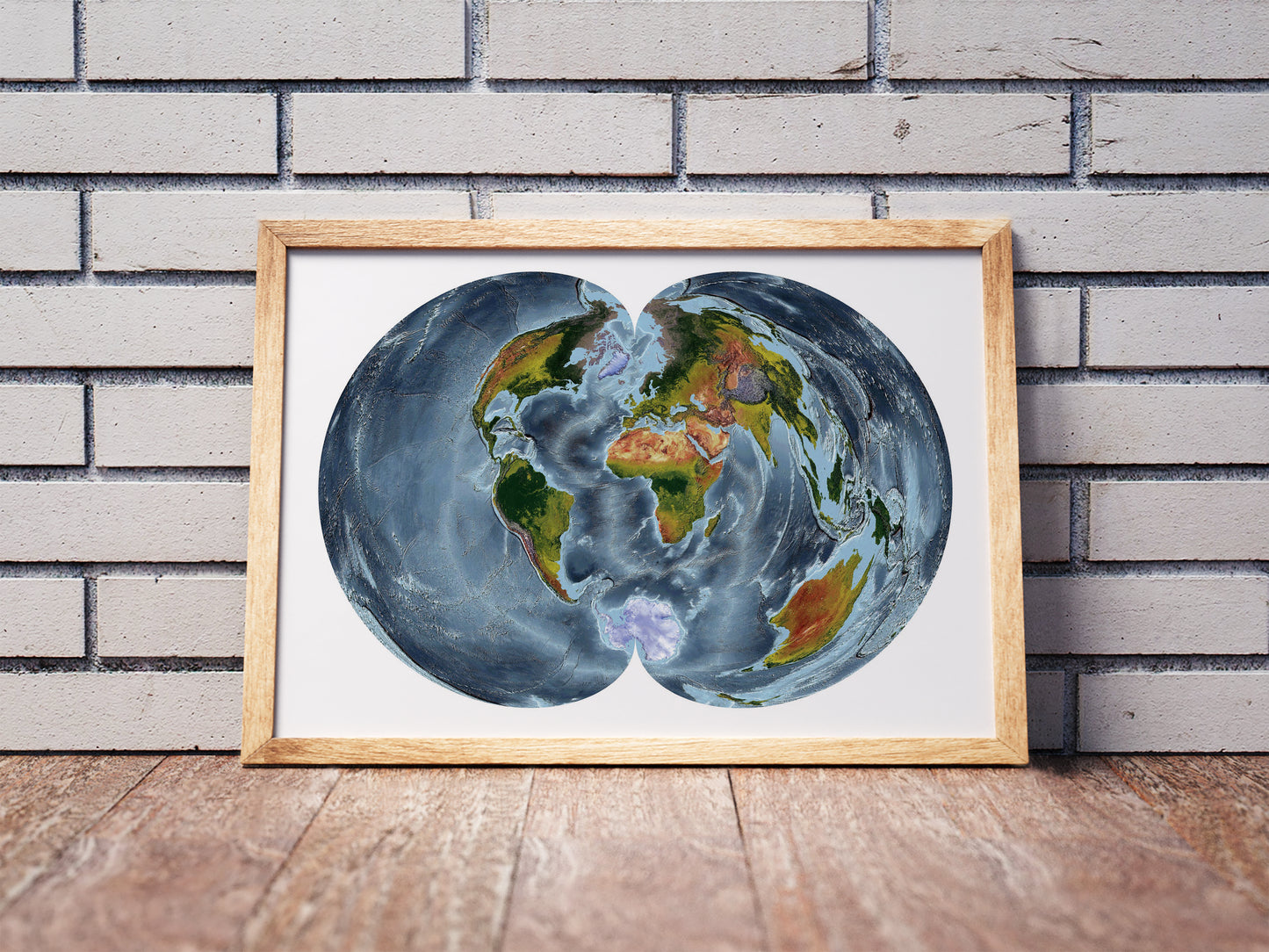 Polyconic projection shaded relief world map in a wooden frame. Realistic terrain art print for home decor, displayed against a brick wall