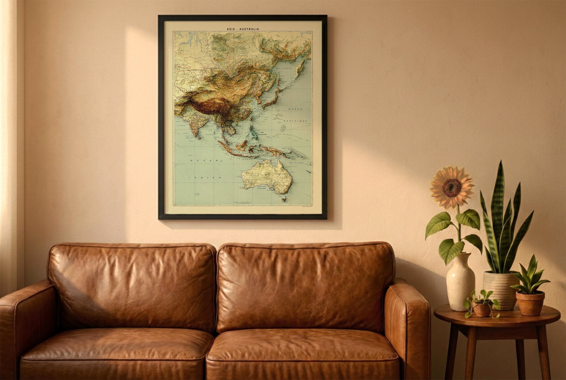 Asia and Australia vintage relief map in a black frame above a brown leather sofa. Boho living room with warm sunlight, sunflower, and indoor plants on a wooden side table