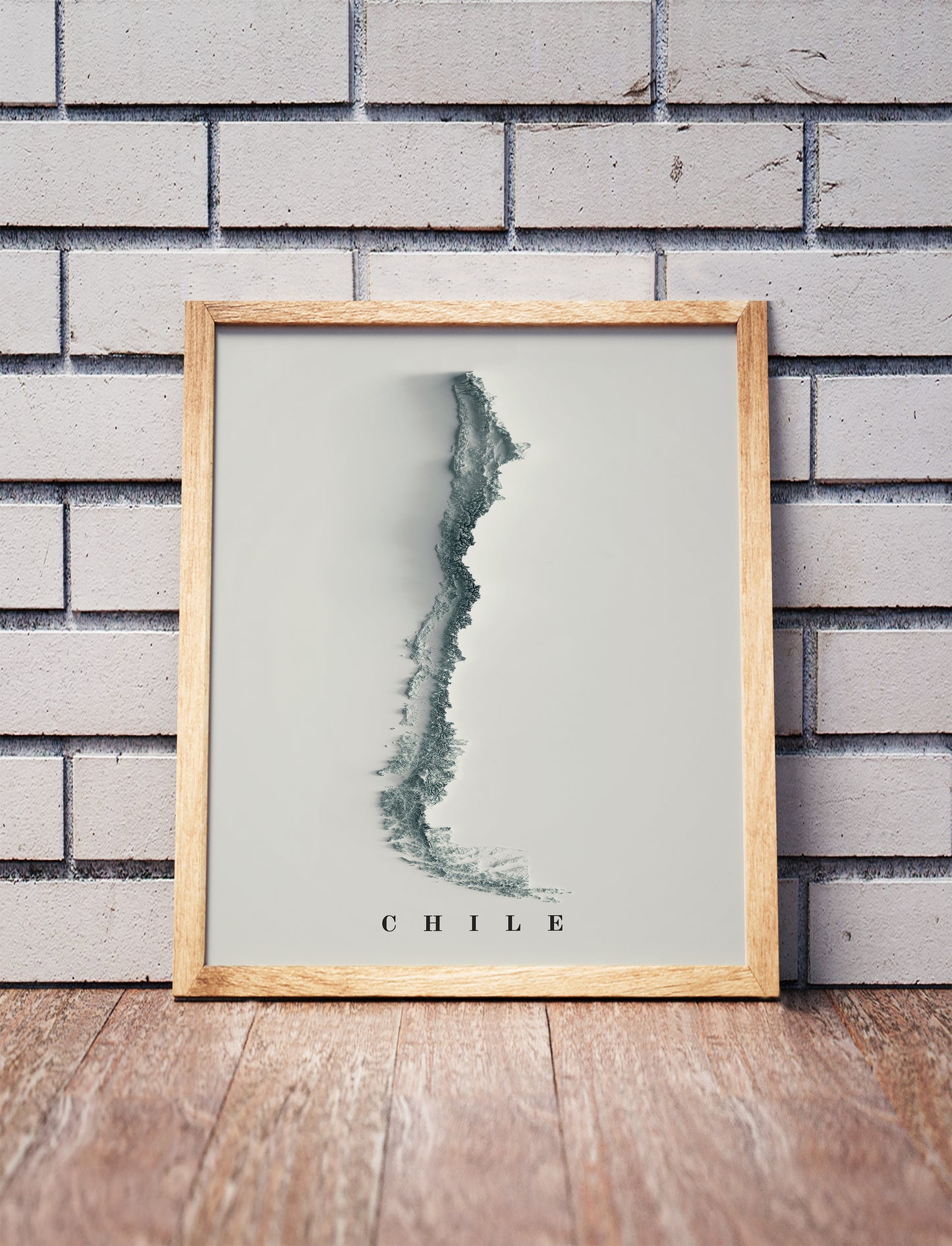 Chile shaded relief map in a wooden frame. Realistic terrain art print for home decor, displayed against a brick wall