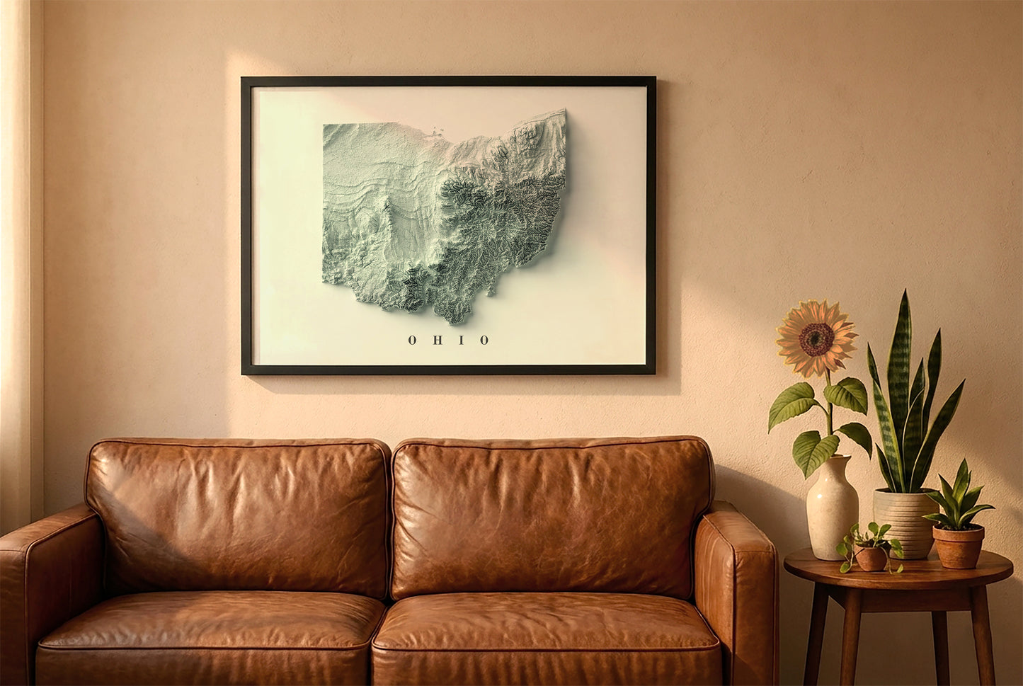Ohio relief map in a black frame above a brown leather sofa. Boho living room with warm sunlight, sunflower, and indoor plants on a wooden side table