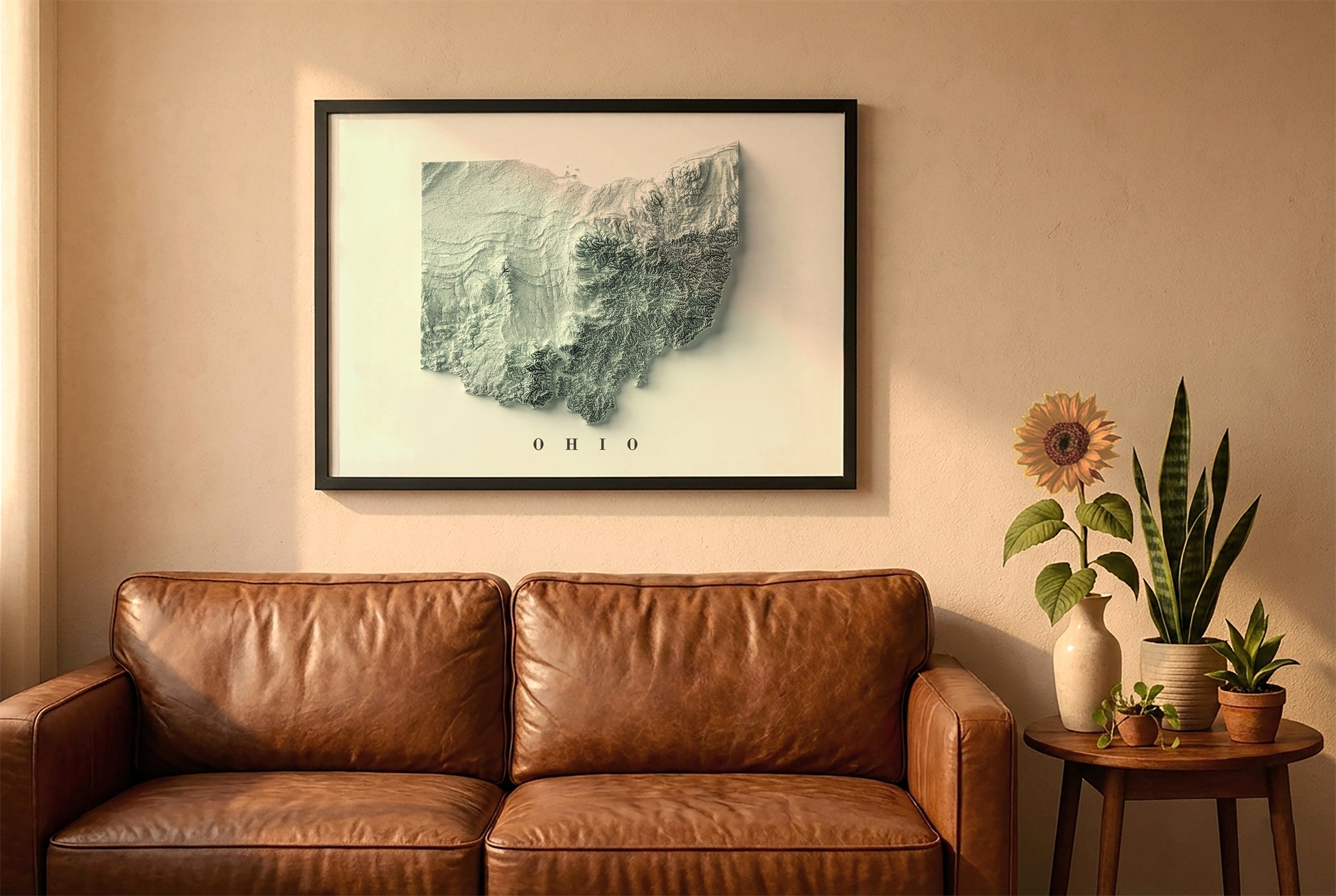 Ohio relief map in a black frame above a brown leather sofa. Boho living room with warm sunlight, sunflower, and indoor plants on a wooden side table