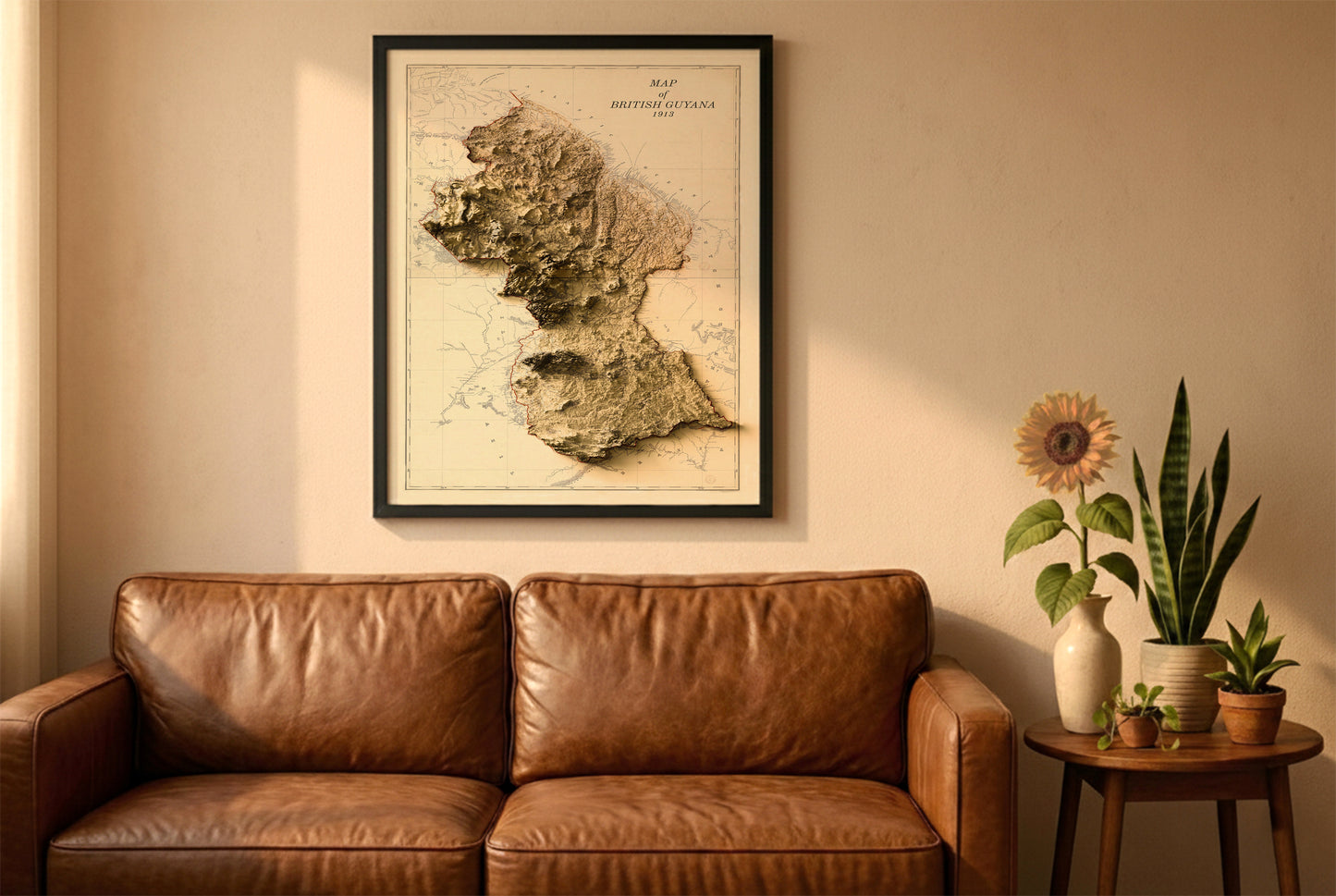 Guyana vintage relief map in a black frame above a brown leather sofa. Boho living room with warm sunlight, sunflower, and indoor plants on a wooden side table