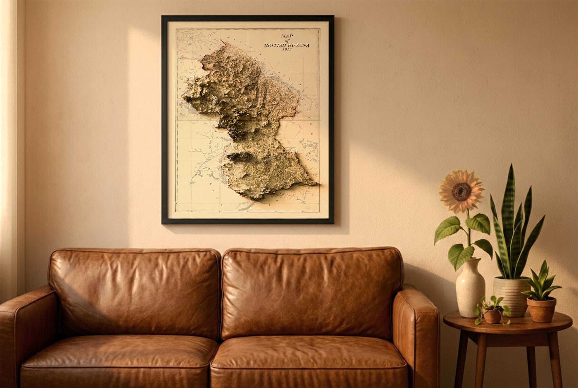 Guyana vintage relief map in a black frame above a brown leather sofa. Boho living room with warm sunlight, sunflower, and indoor plants on a wooden side table