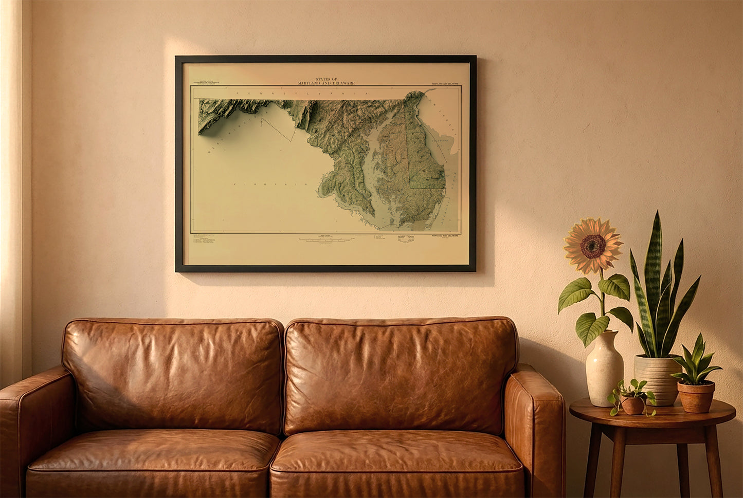 Maryland vintage relief map in a black frame above a brown leather sofa. Boho living room with warm sunlight, sunflower, and indoor plants on a wooden side table