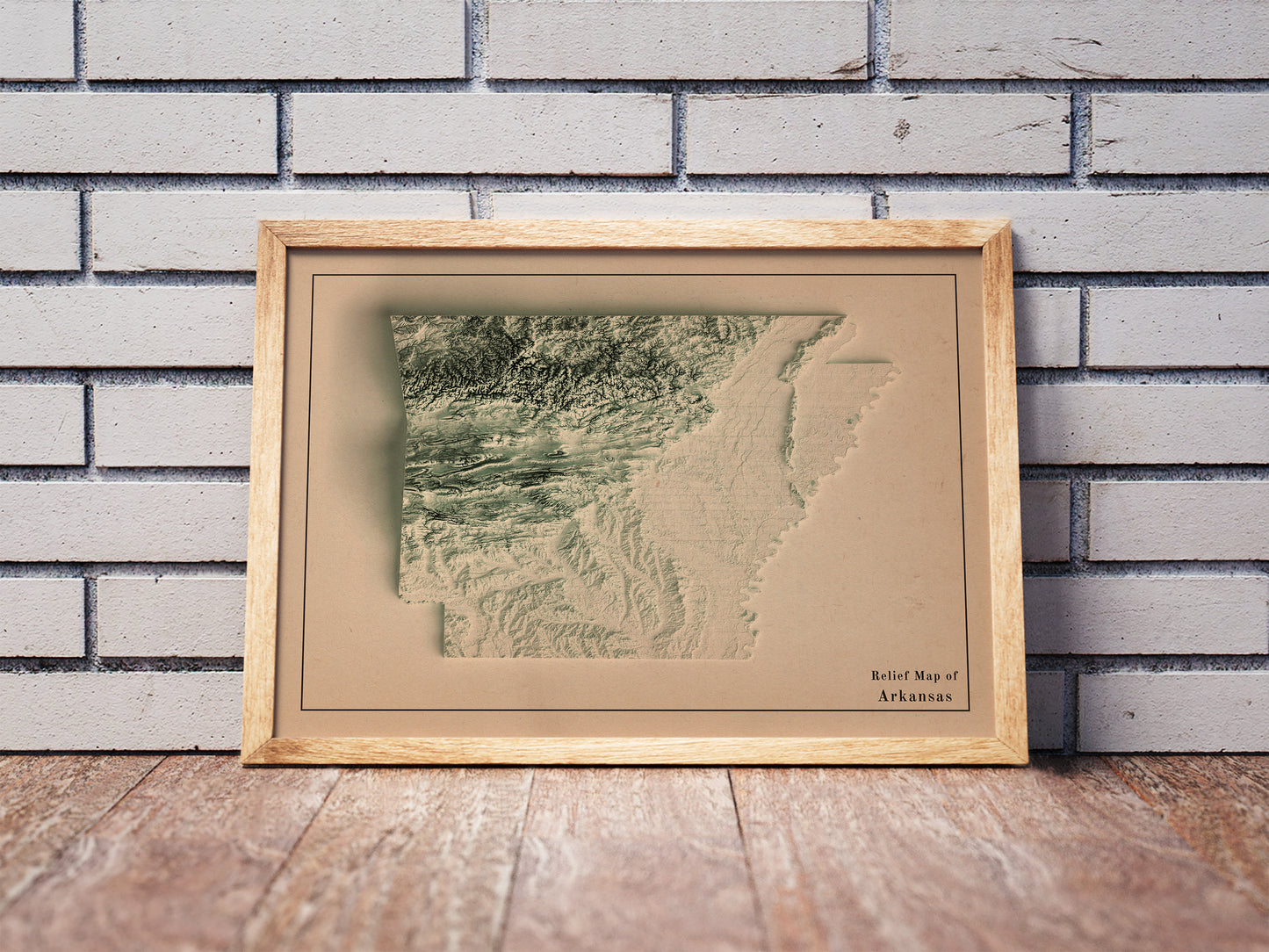Vintage Arkansas shaded relief map in a wooden frame. Realistic terrain art print for home decor, displayed against a brick wall