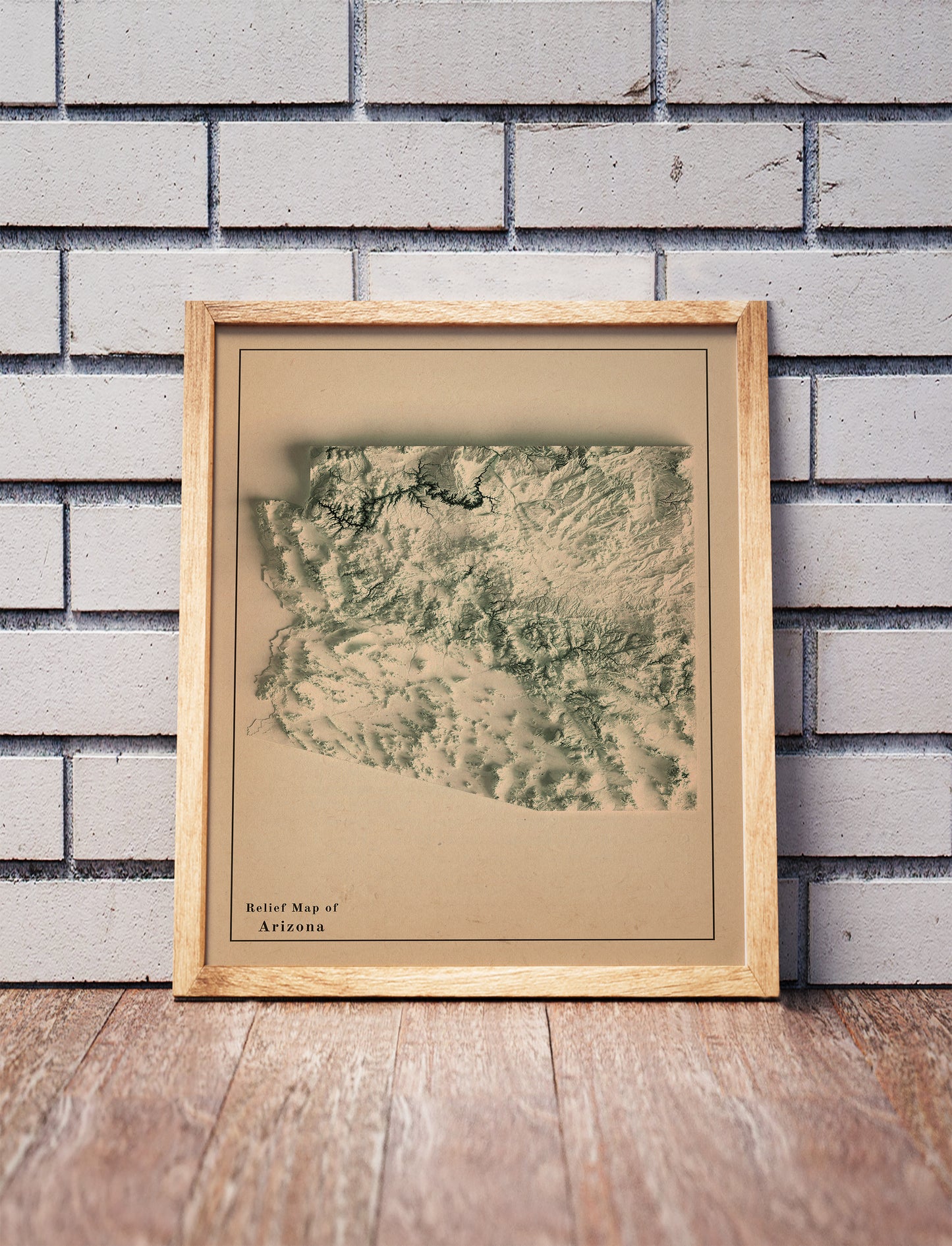 Vintage Arizona shaded relief map in a wooden frame. Realistic terrain art print for home decor, displayed against a brick wall