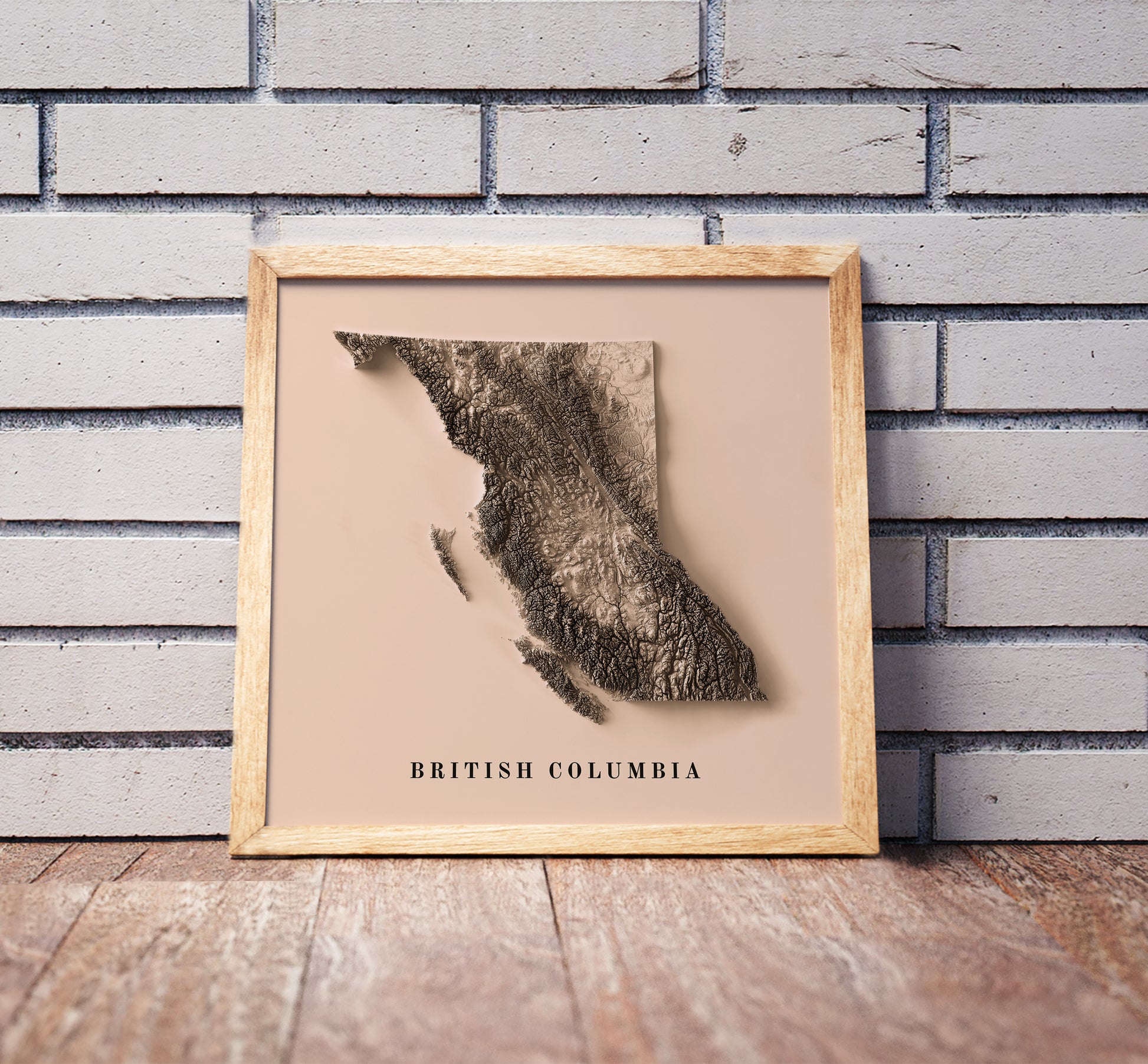 British Columbia, Canada, shaded relief map in a wooden frame. Realistic terrain art print for home decor, displayed against a brick wall