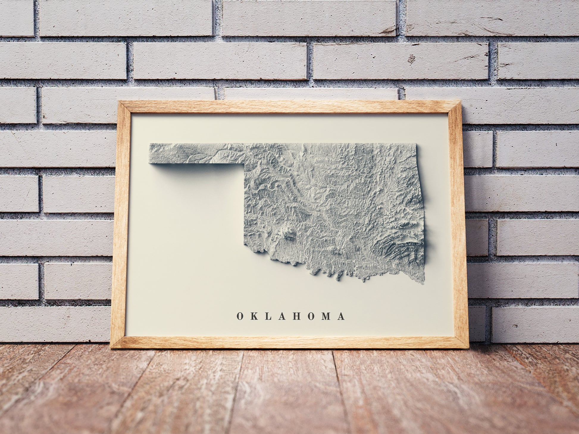 Oklahoma shaded relief map in a wooden frame. Realistic terrain art print for home decor, displayed against a brick wall