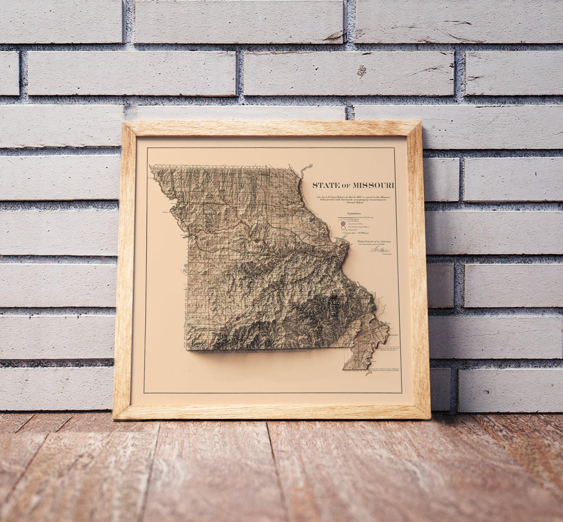 Vintage Missouri shaded relief map in a wooden frame. Realistic terrain art print for home decor, displayed against a brick wall