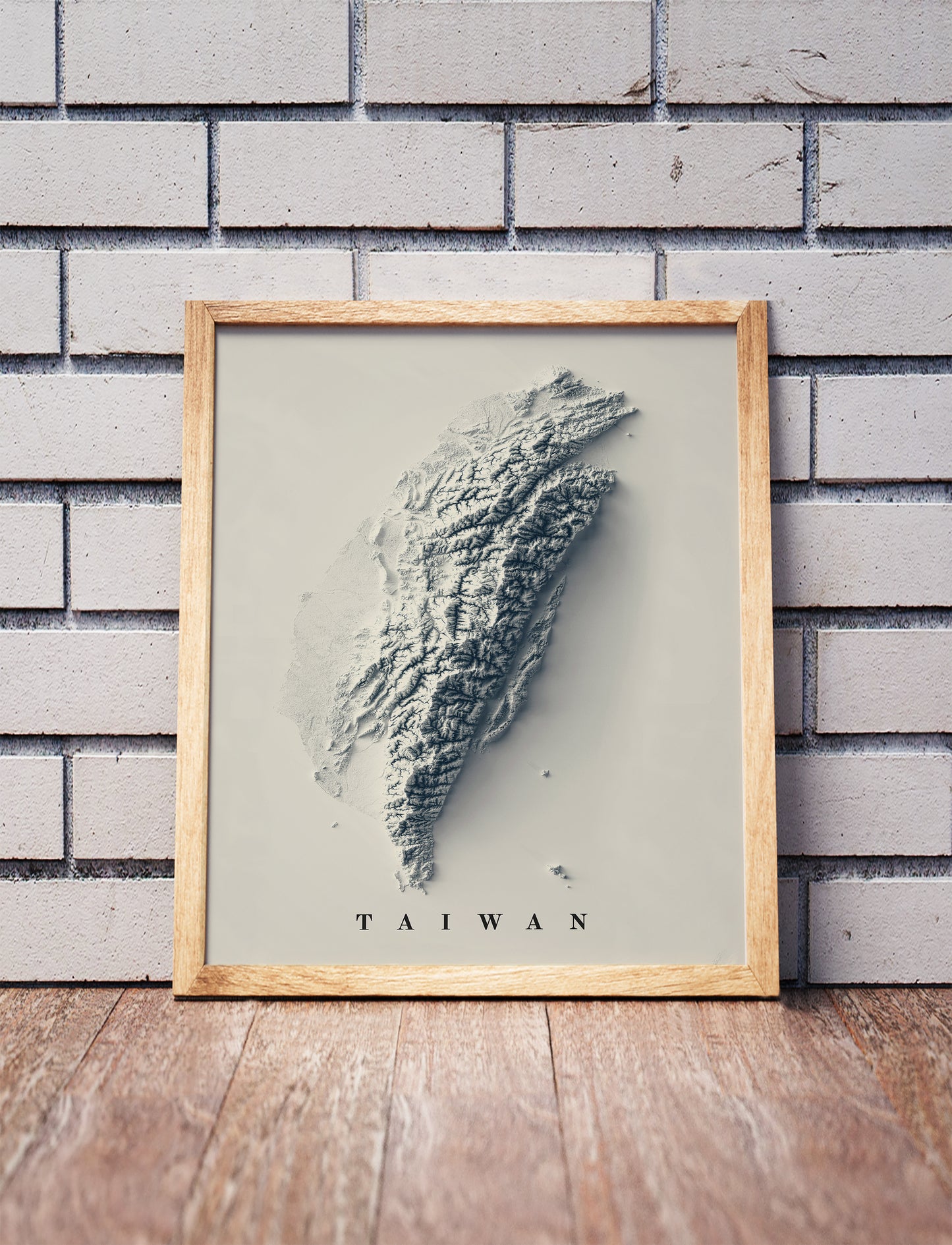 Taiwan shaded relief map in a wooden frame. Realistic terrain art print for home decor, displayed against a brick wall