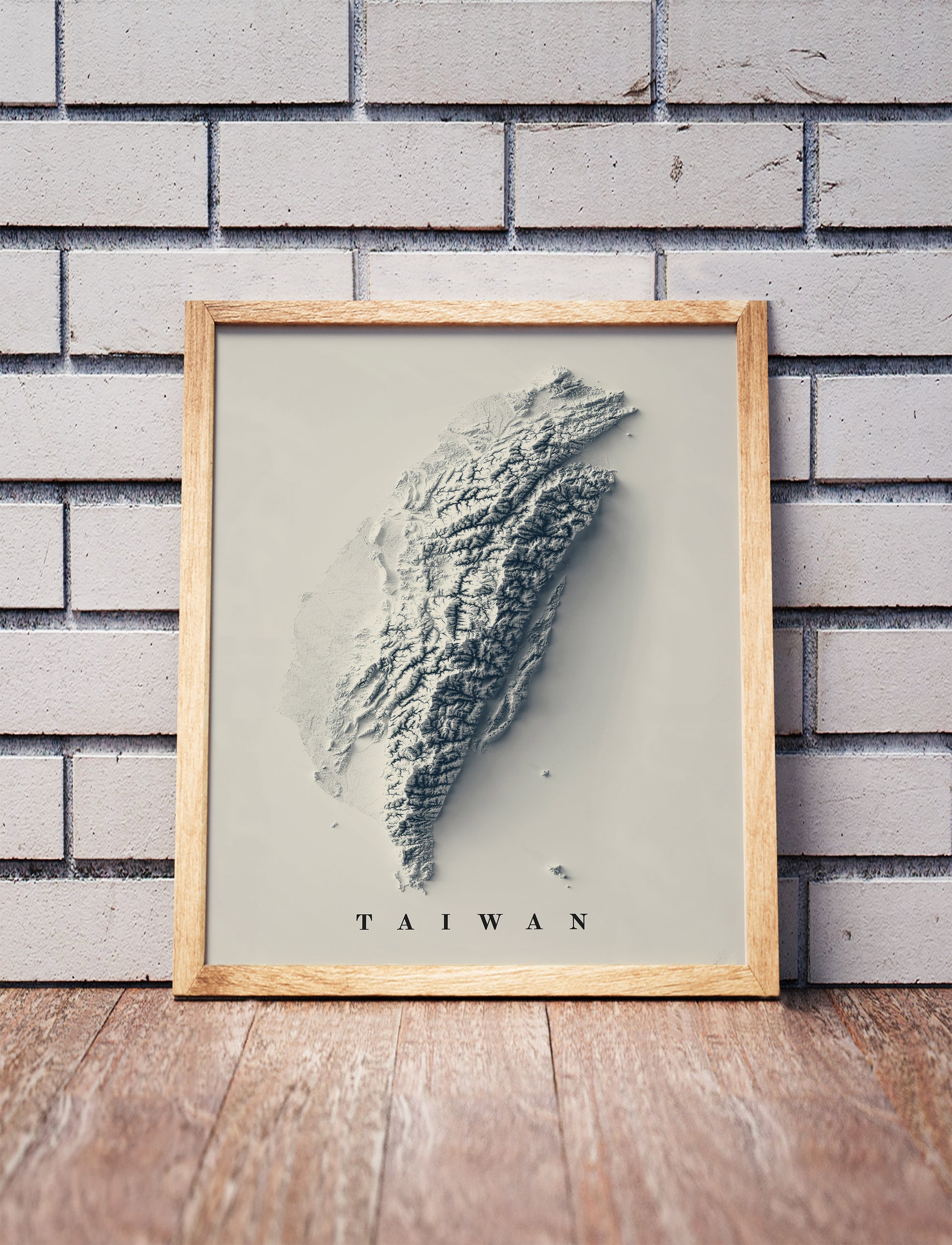 Taiwan shaded relief map in a wooden frame. Realistic terrain art print for home decor, displayed against a brick wall