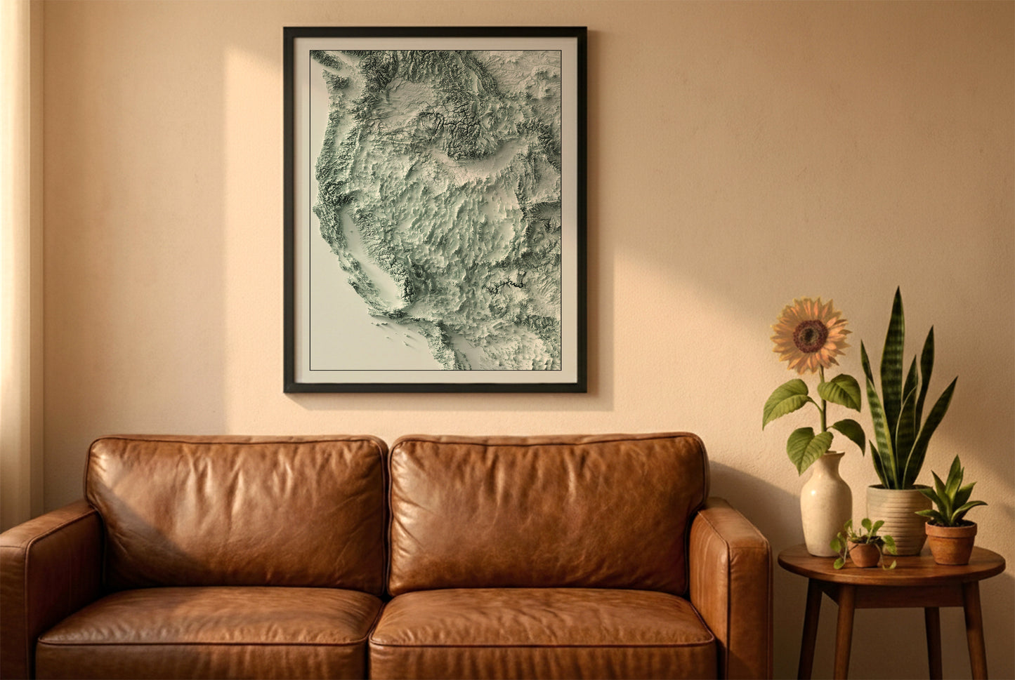Western USA relief map in a black frame above a brown leather sofa. Boho living room with warm sunlight, sunflower, and indoor plants on a wooden side table