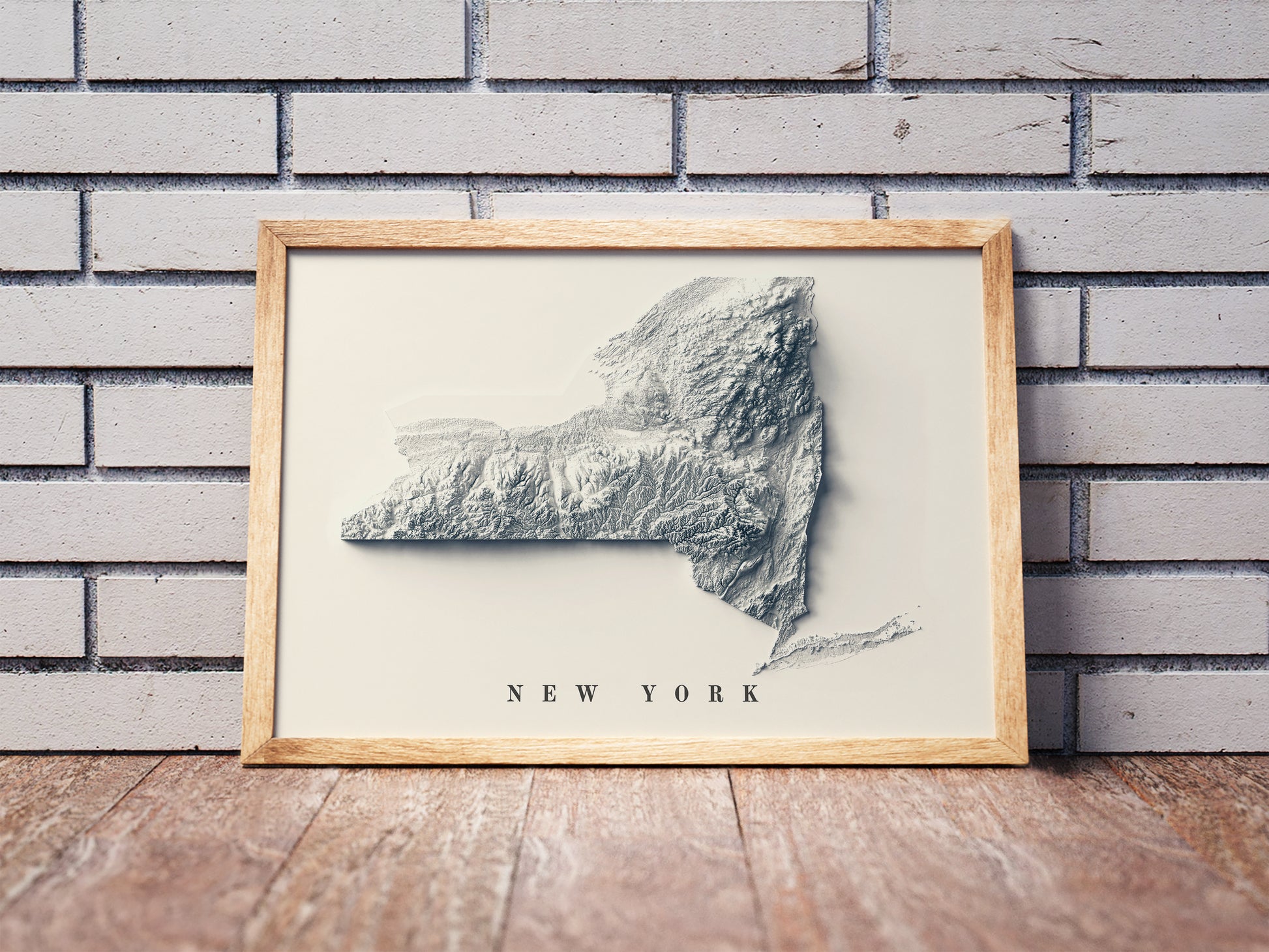 New York state shaded relief map in a wooden frame. Realistic terrain art print for home decor, displayed against a brick wall