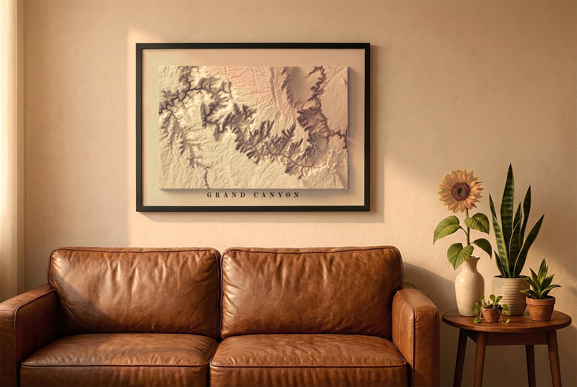 Grand Canyon relief map in a black frame above a brown leather sofa. Boho living room with warm sunlight, sunflower, and indoor plants on a wooden side table