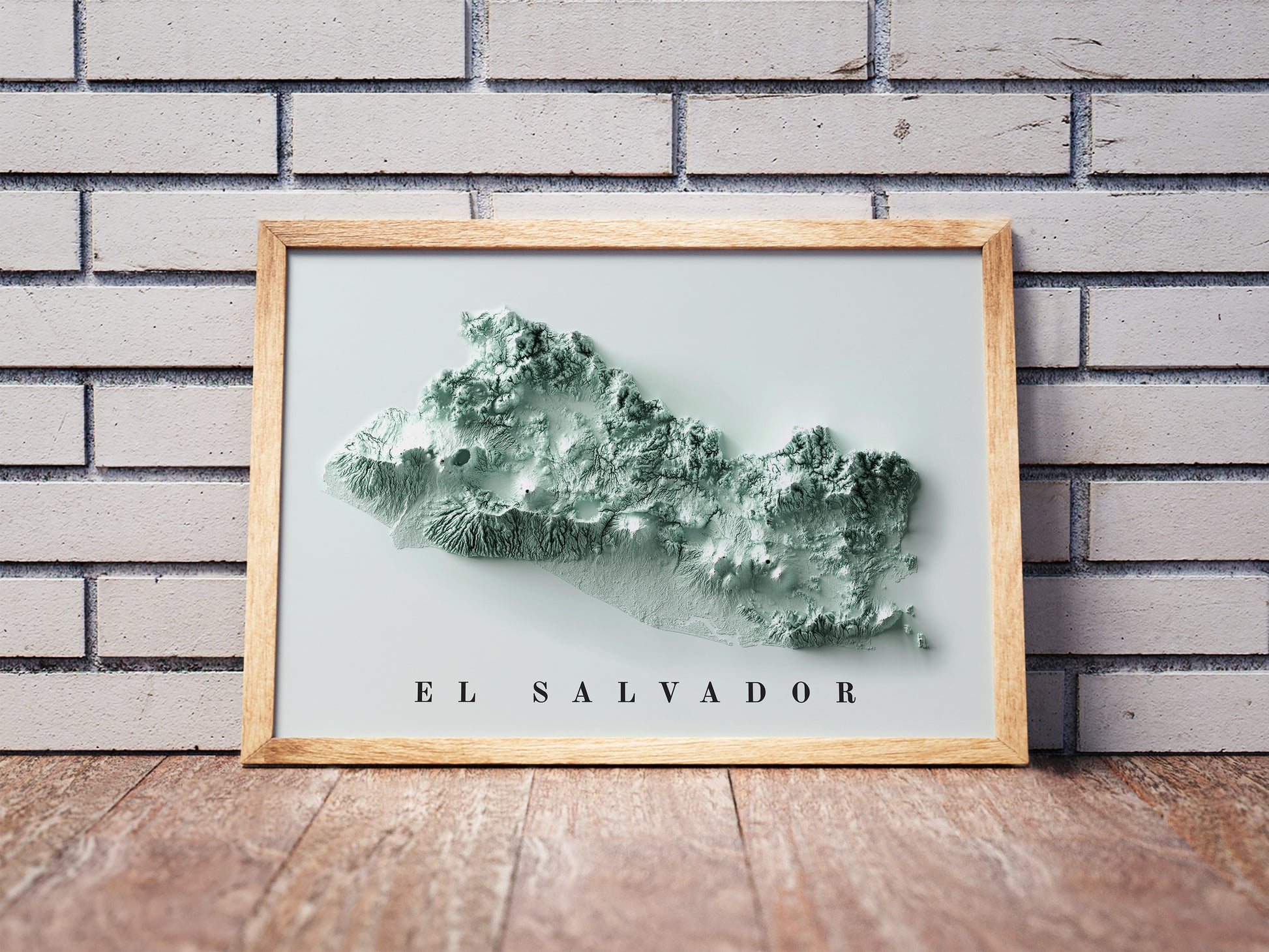 El Salvador shaded relief map in a wooden frame. Realistic terrain art print for home decor, displayed against a brick wall