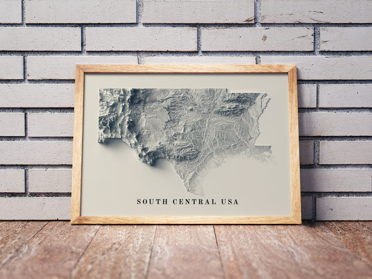 South Central USA shaded relief map in a wooden frame. Realistic terrain art print for home decor, displayed against a brick wall