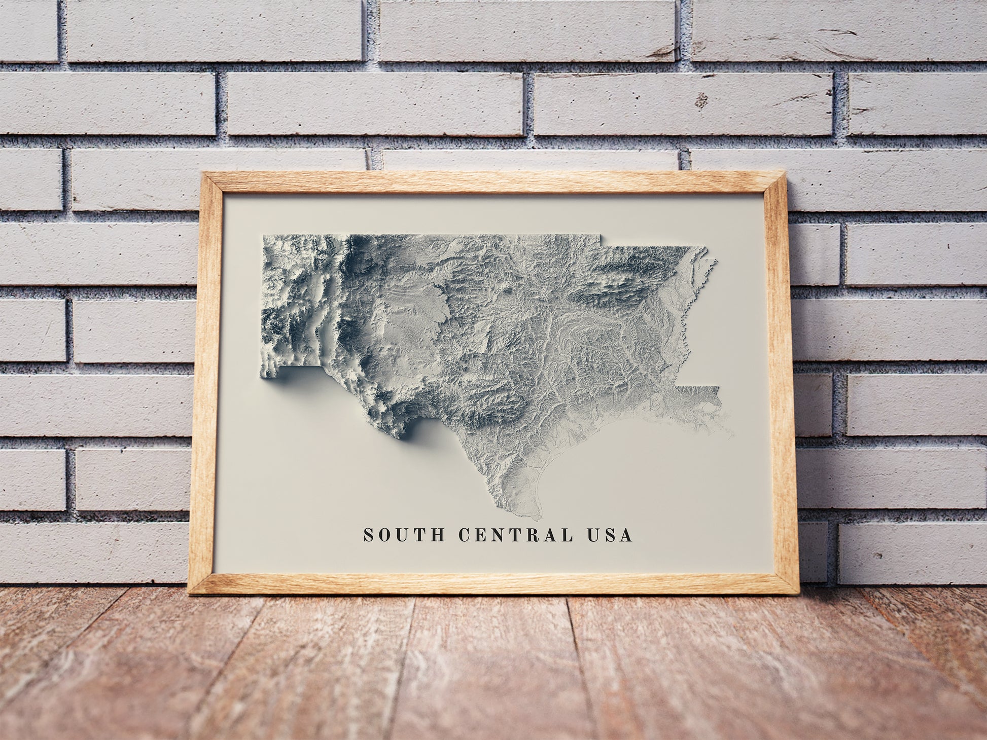 South Central USA shaded relief map in a wooden frame. Realistic terrain art print for home decor, displayed against a brick wall
