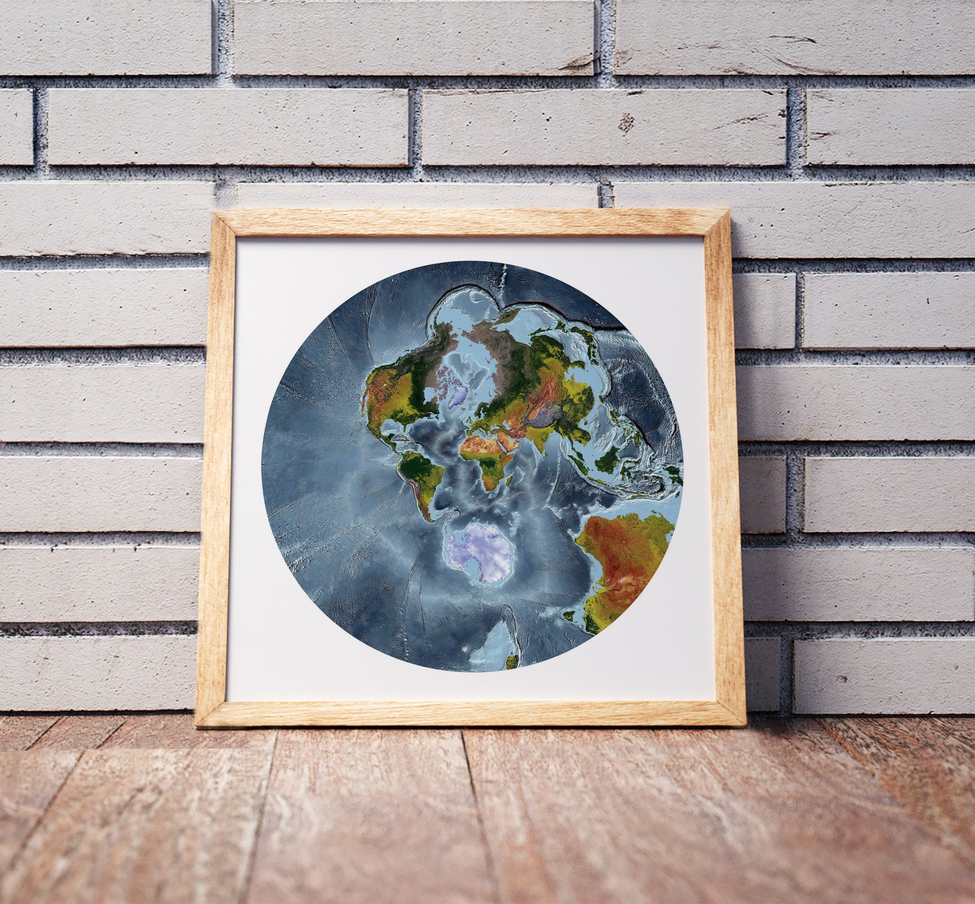 Stereographic projection shaded relief world map in a wooden frame. Realistic terrain art print for home decor, displayed against a brick wall