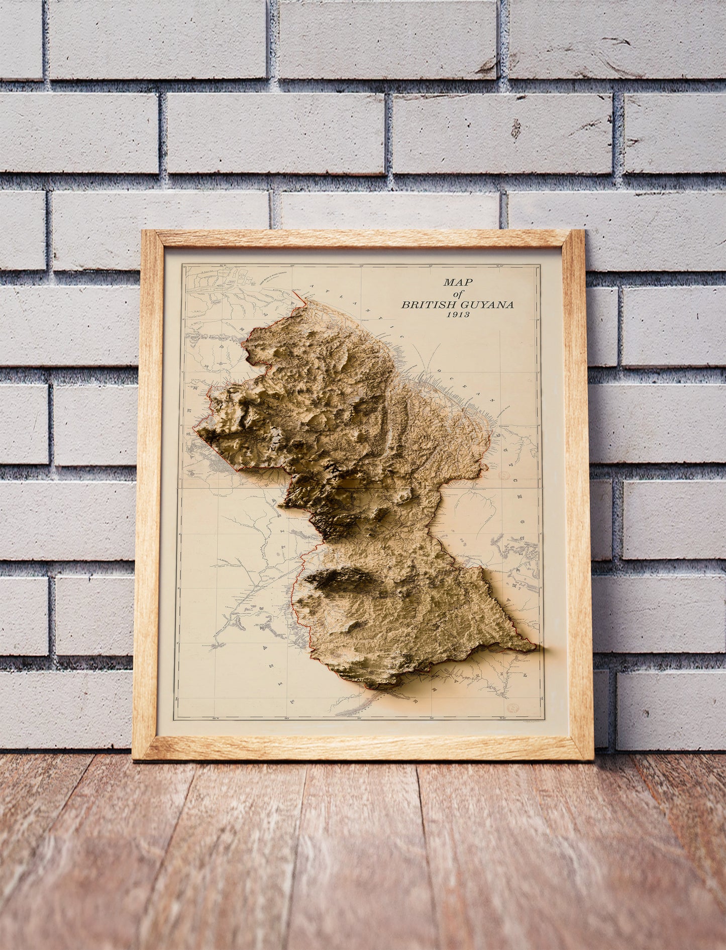 Vintage Guyana shaded relief map in a wooden frame. Realistic terrain art print for home decor, displayed against a brick wall