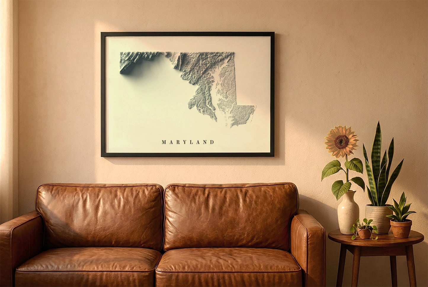 Maryland relief map in a black frame above a brown leather sofa. Boho living room with warm sunlight, sunflower, and indoor plants on a wooden side table