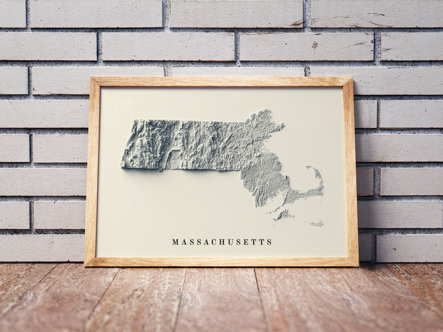 Massachusetts shaded relief map in a wooden frame. Realistic terrain art print for home decor, displayed against a brick wall