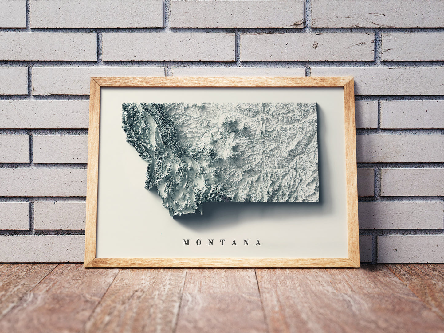 Montana shaded relief map in a wooden frame. Realistic terrain art print for home decor, displayed against a brick wall