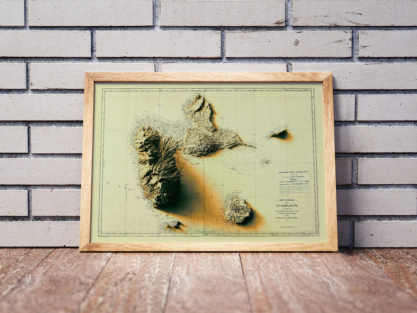 Vintage Guadeloupe, France, shaded relief map in a wooden frame. Realistic terrain art print for home decor, displayed against a brick wall