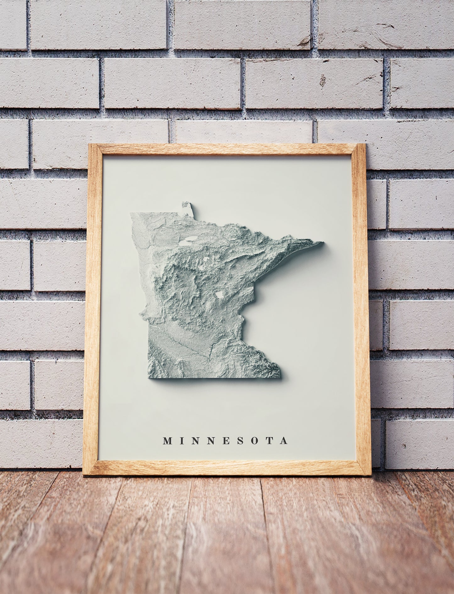 Minnesota shaded relief map in a wooden frame. Realistic terrain art print for home decor, displayed against a brick wall